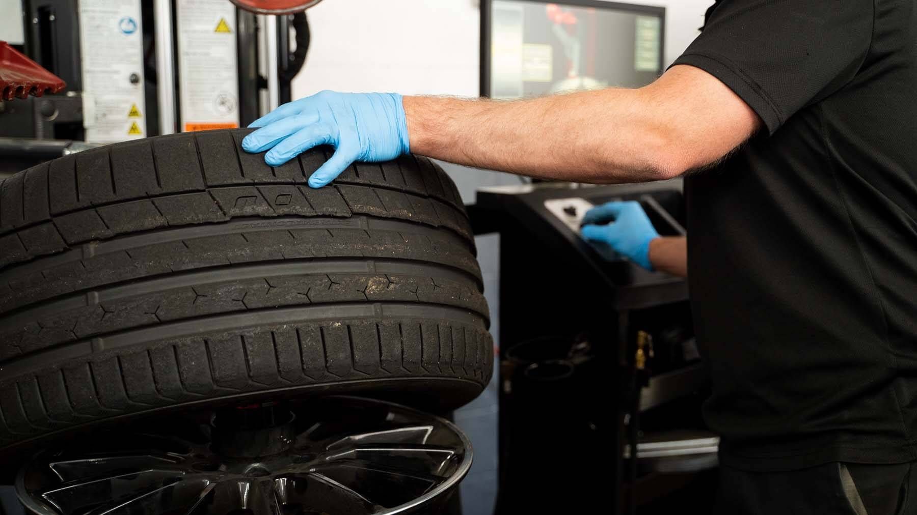 A man wearing blue gloves is working on a tire in a garage. | The Euro Shop