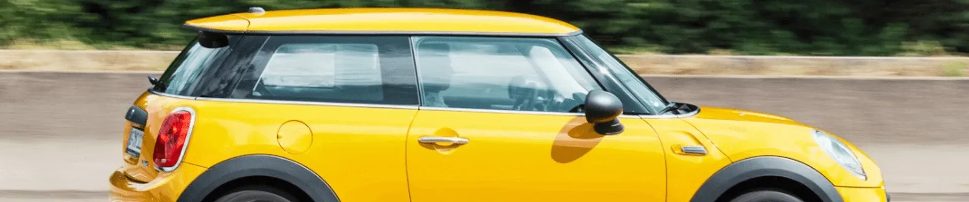 A yellow mini cooper is driving down a road. | The Euro Shop