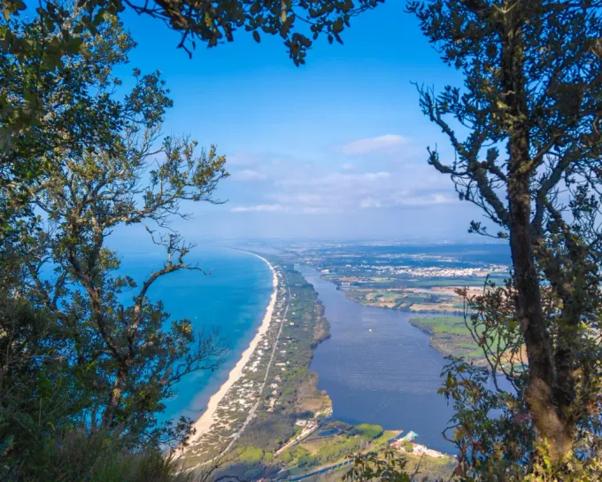 Veduta aerea costiera di una stretta spiaggia, dell'oceano blu e di un corso d'acqua interno incorniciato dagli alberi.