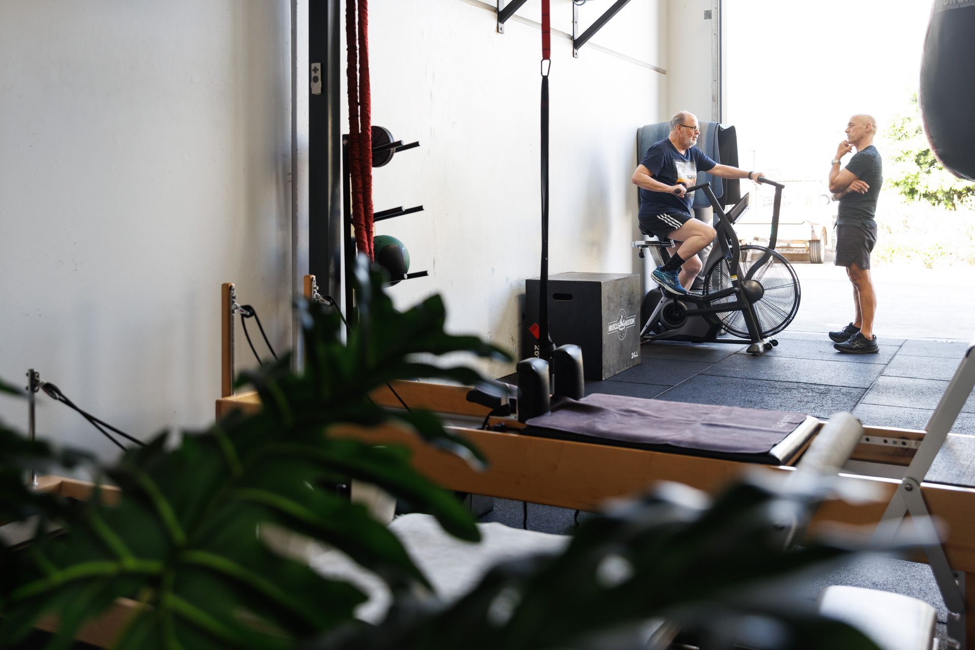 Pilates studio with Chris Massey training a customer on an assault bike.