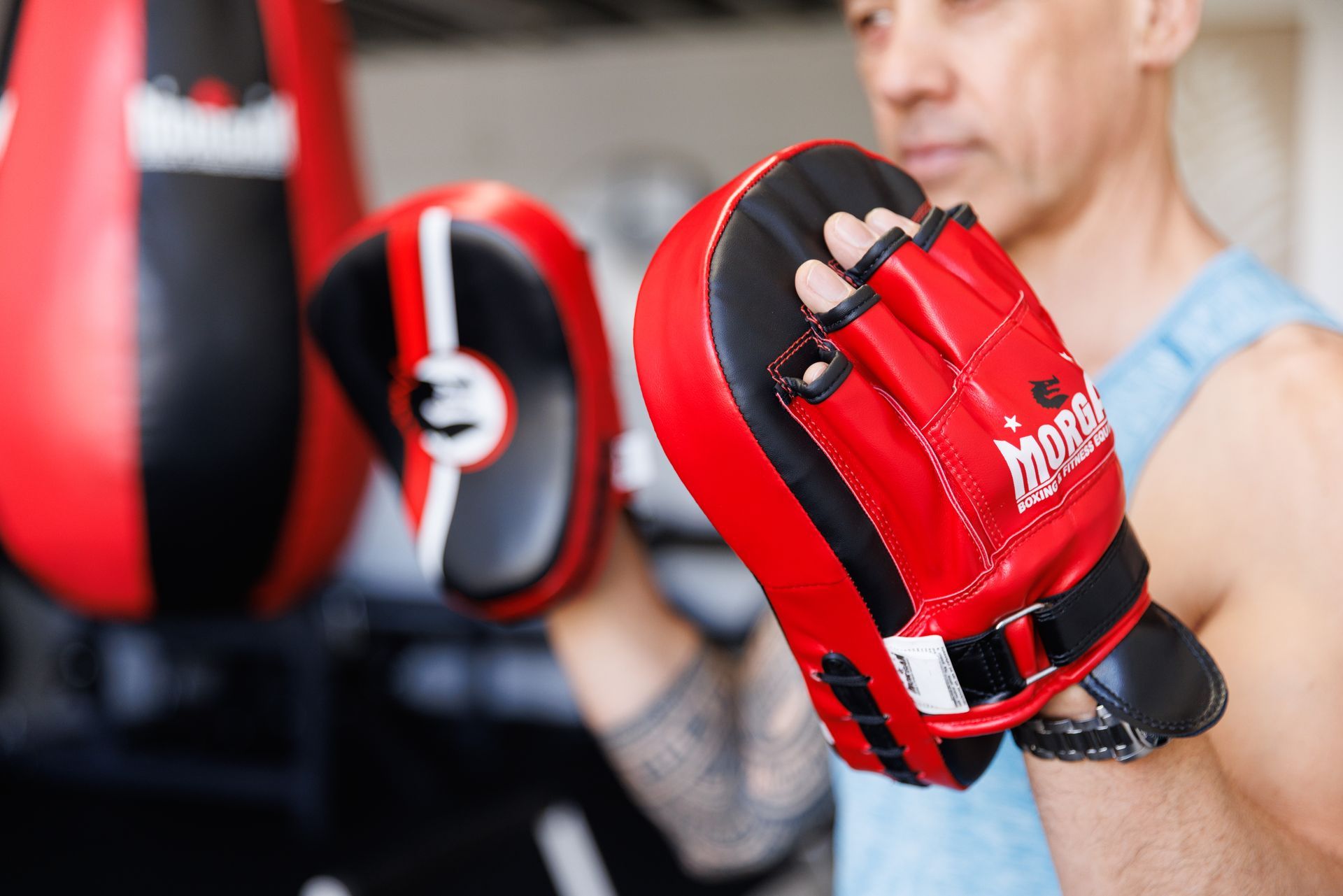 Man wearing red and black boxing mitts, with a punching bag in background.