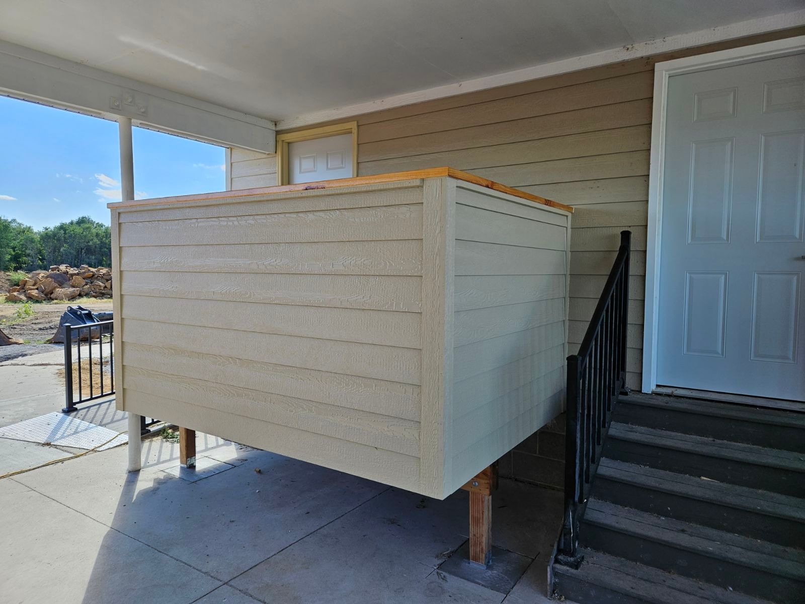 A large wooden box is sitting on the side of a house next to stairs.