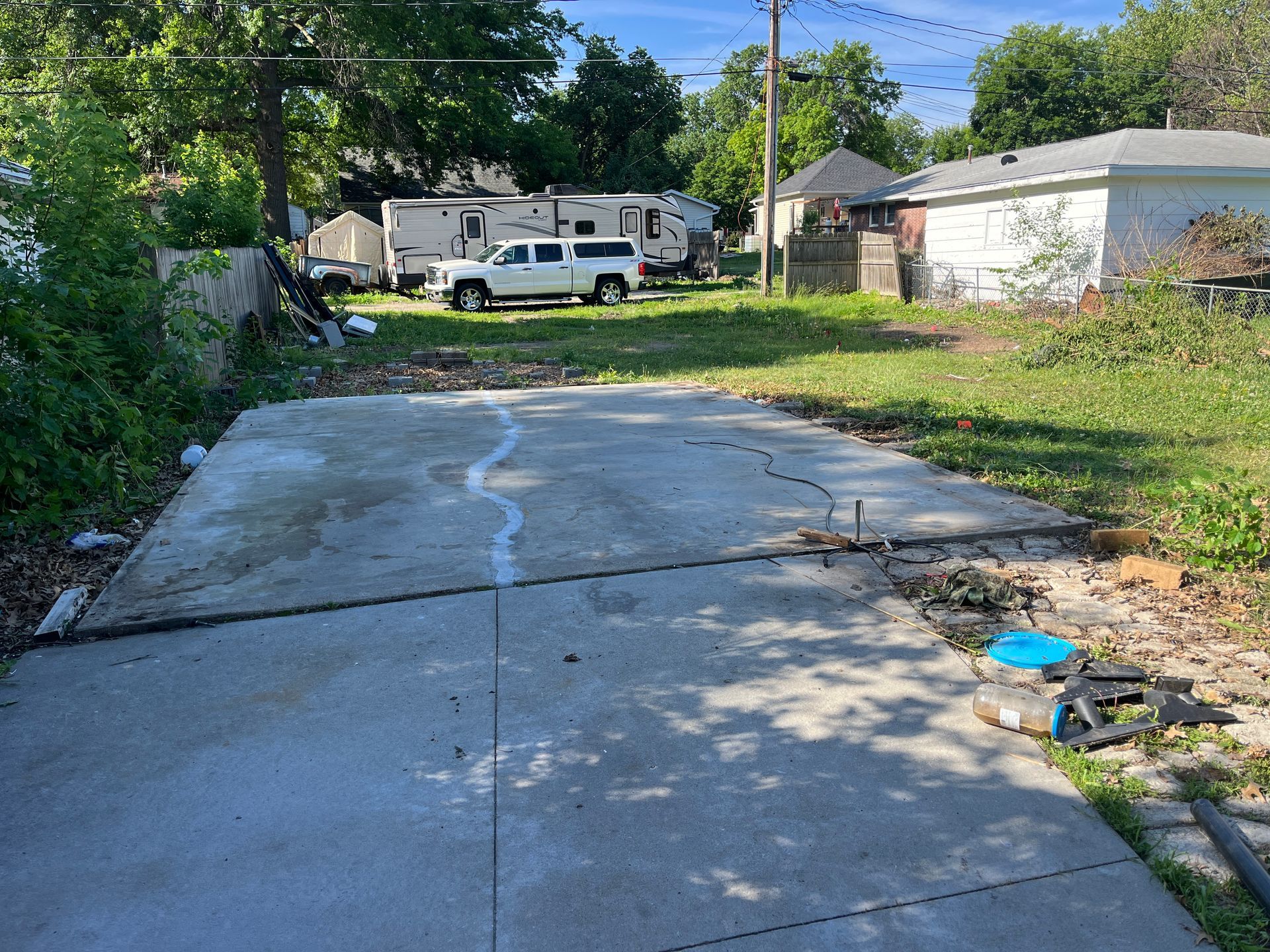 Concrete slab in foreground with a cracked line. A truck, RVs, and houses are in the background on a grassy lot.