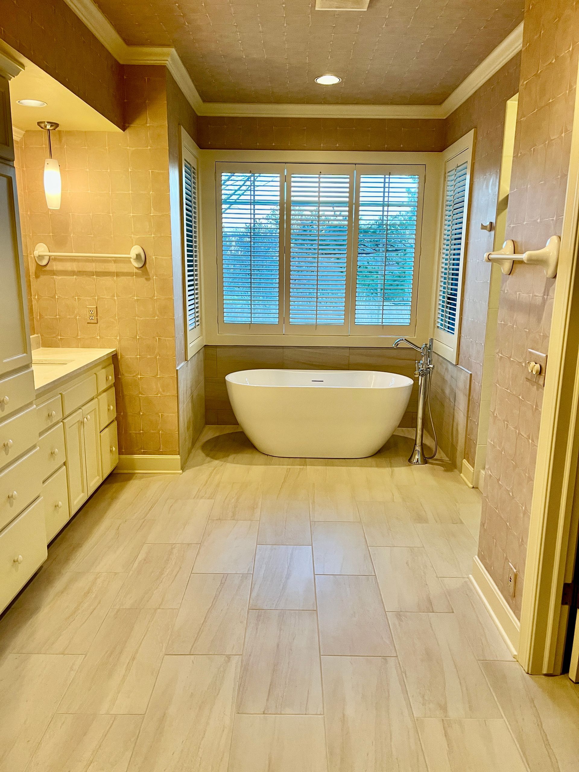 Bathroom with a white tub, light-colored tile floors, and a window with blinds.