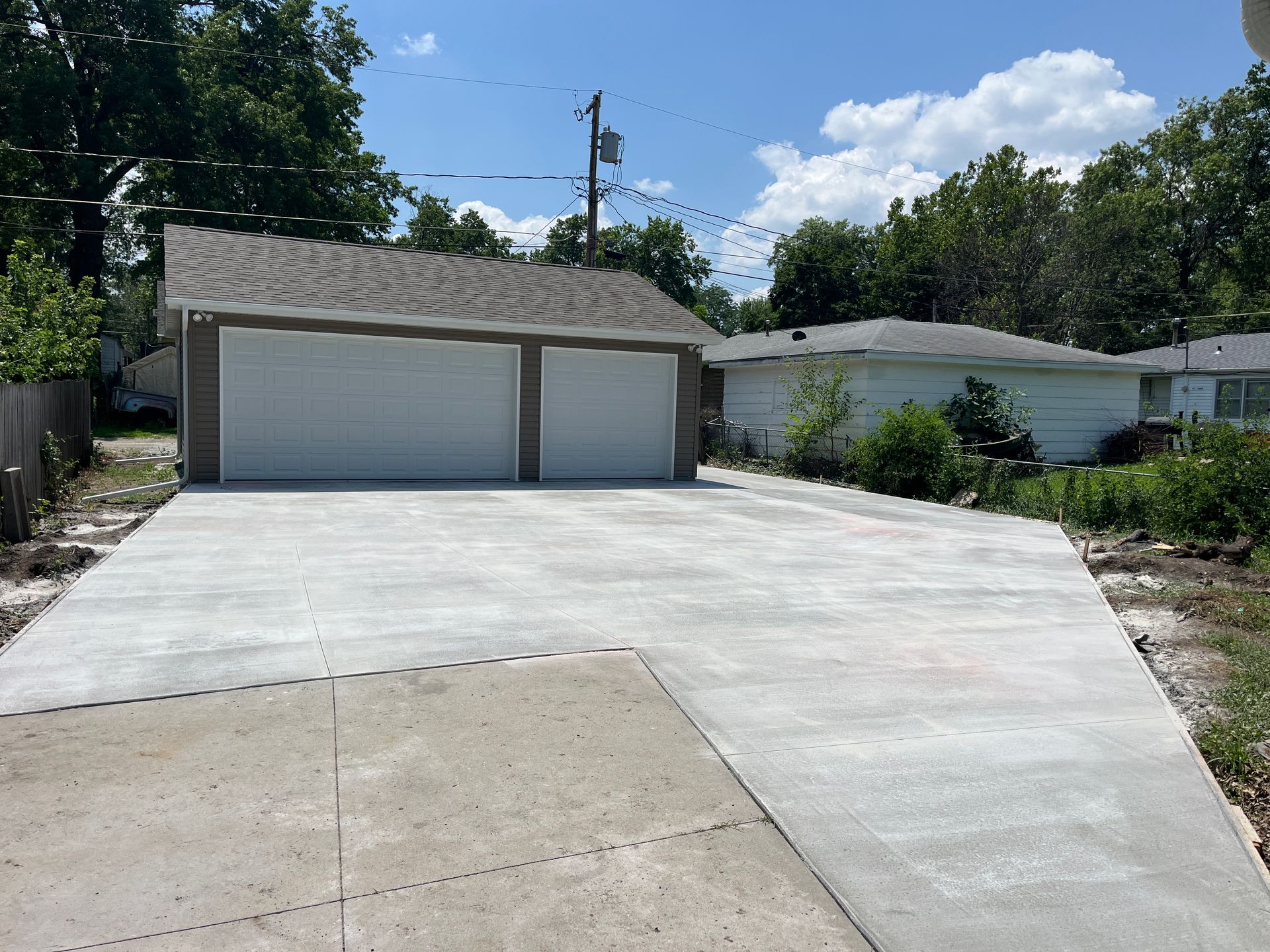 Newly poured concrete driveway leads to a two-car garage with white doors on a sunny day.