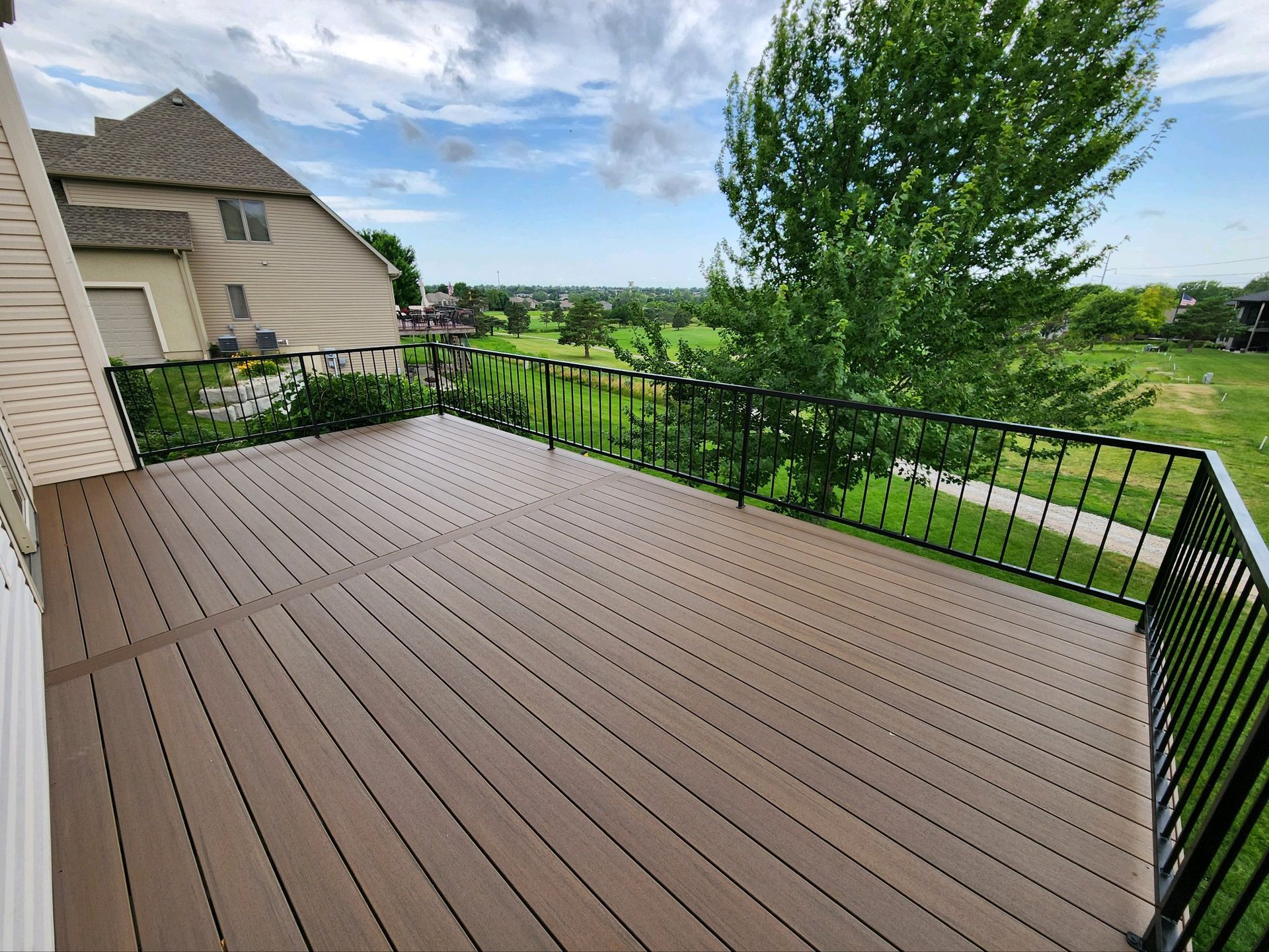 A large wooden deck with a metal railing and a view of a golf course.