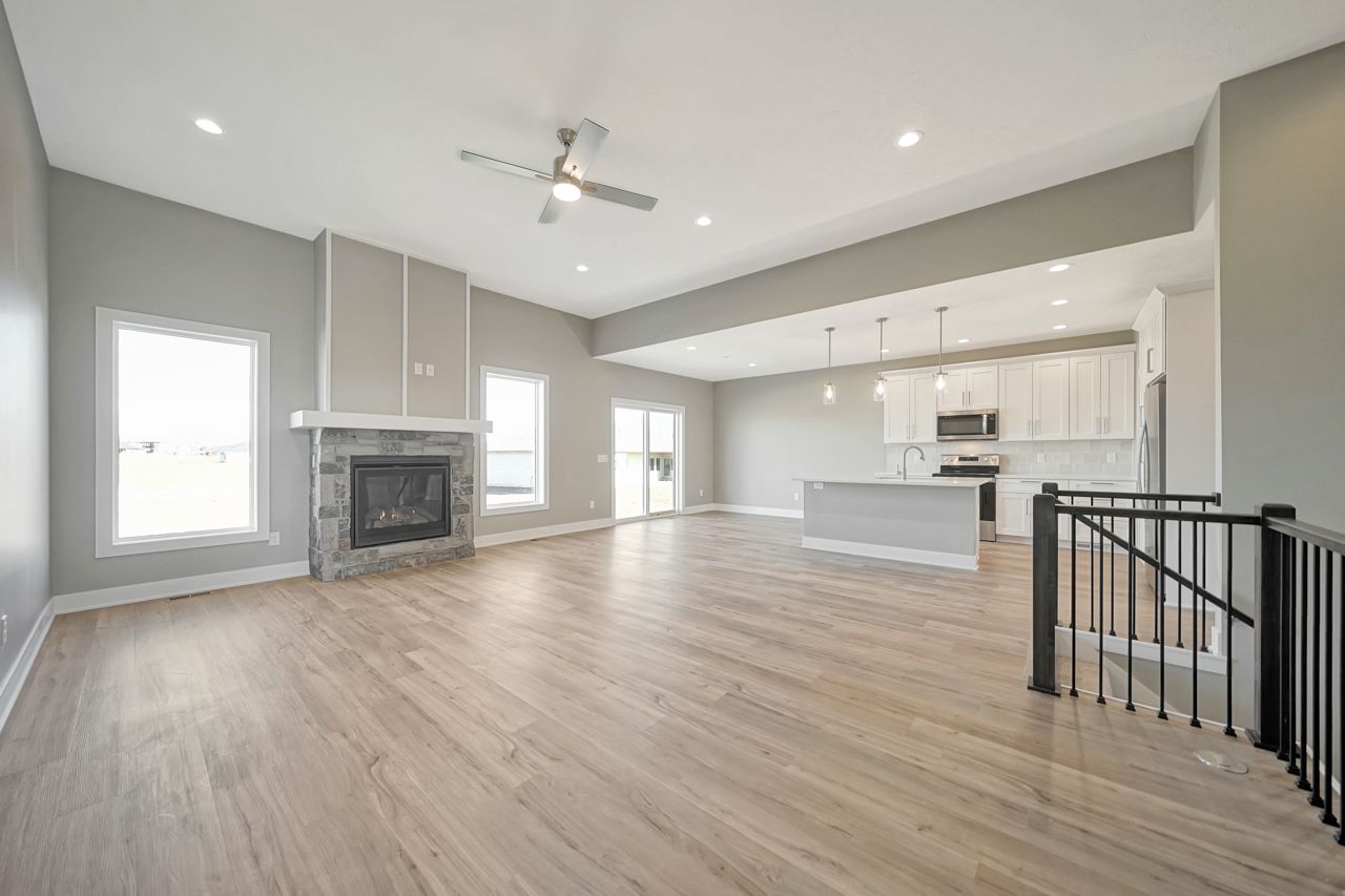 An empty living room with hardwood floors , a fireplace and a ceiling fan.