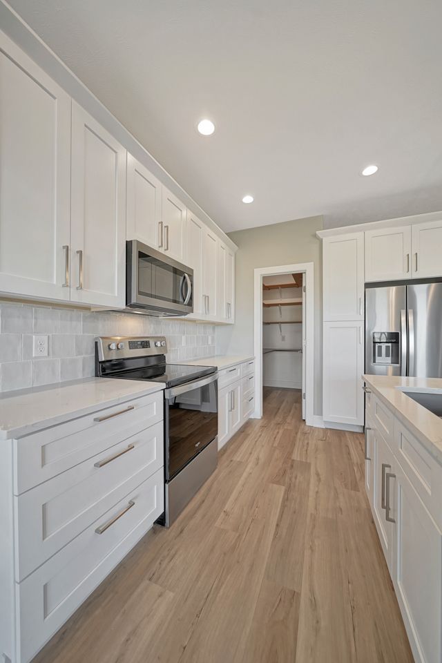 A kitchen with white cabinets , stainless steel appliances , and hardwood floors.