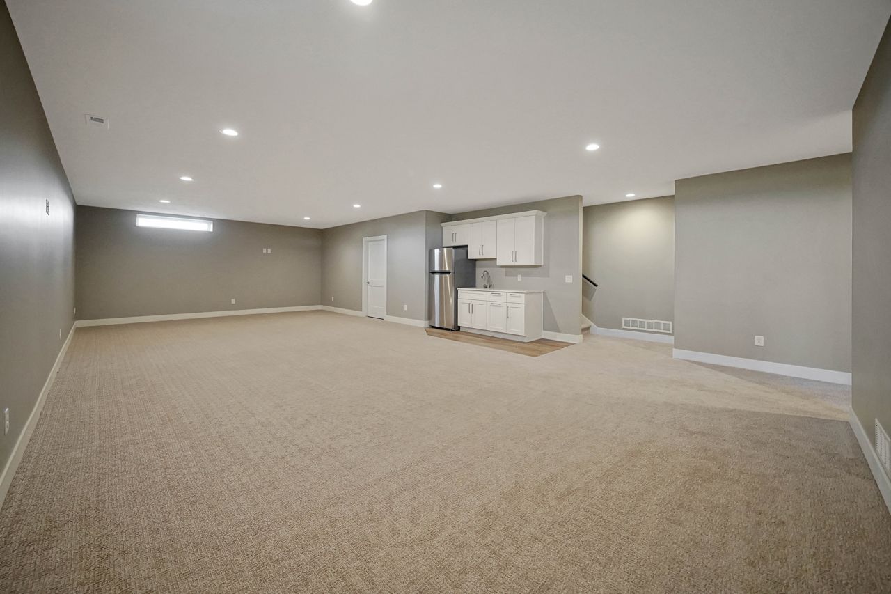 An empty basement with a carpeted floor and a kitchen.