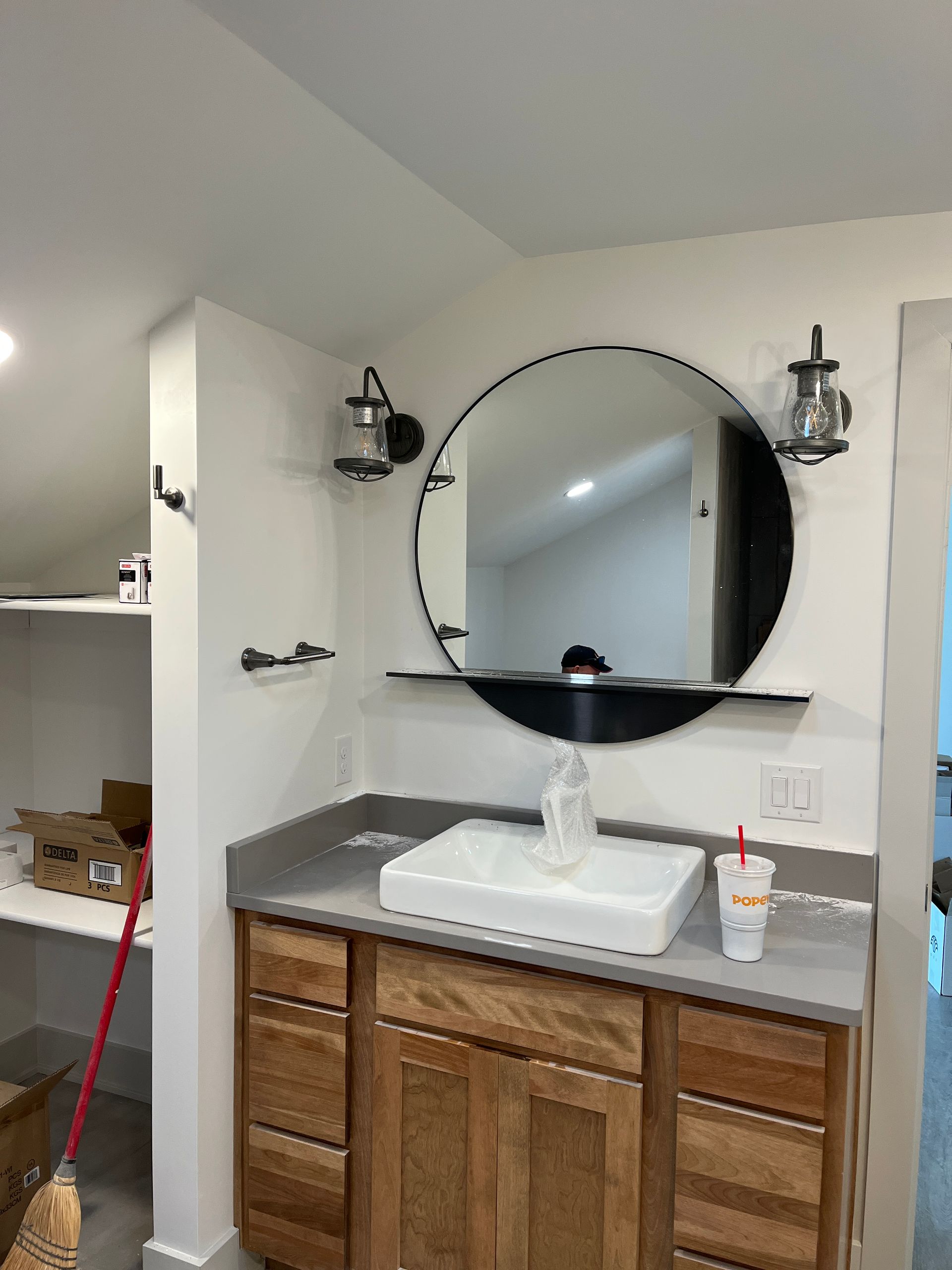 Bathroom vanity with a large round mirror, a wooden cabinet, and a rectangular sink. Wall-mounted sconces flank the mirror.
