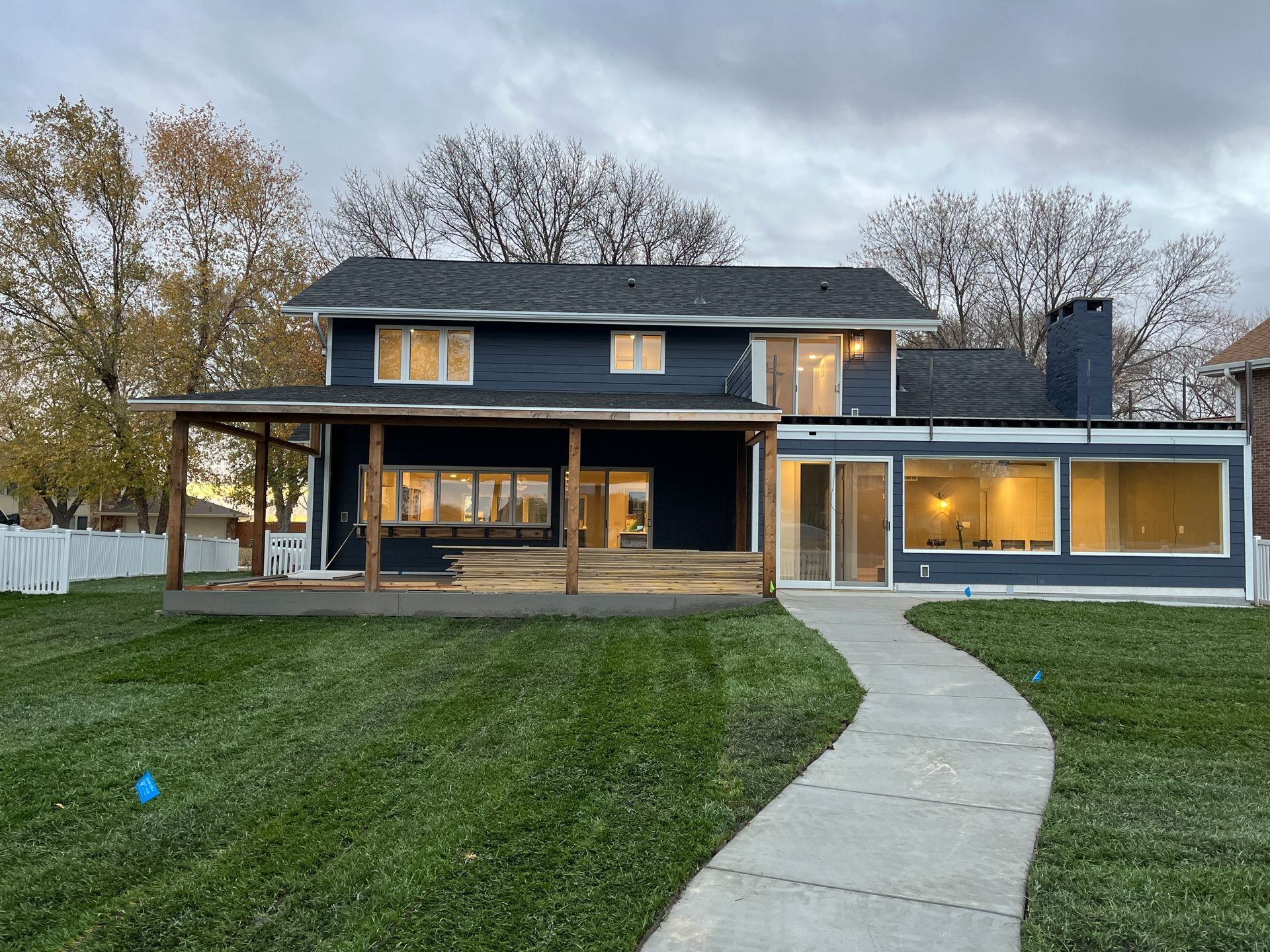 Back of a two-story blue house with a patio and long walkway, on a green lawn under a cloudy sky.