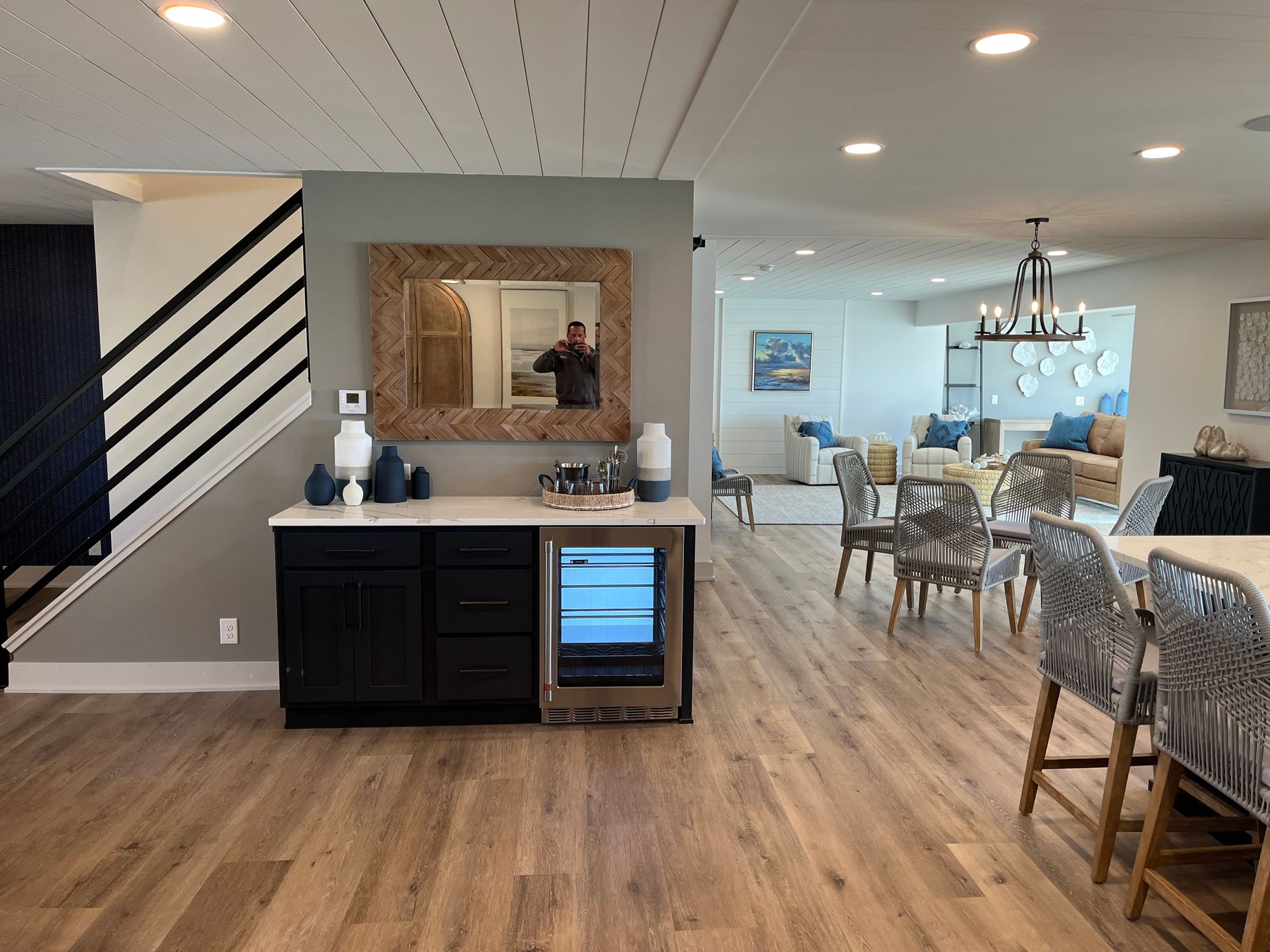 Interior of a modern home featuring a bar area with a mirror and a built-in cooler, and a dining area with patterned chairs.