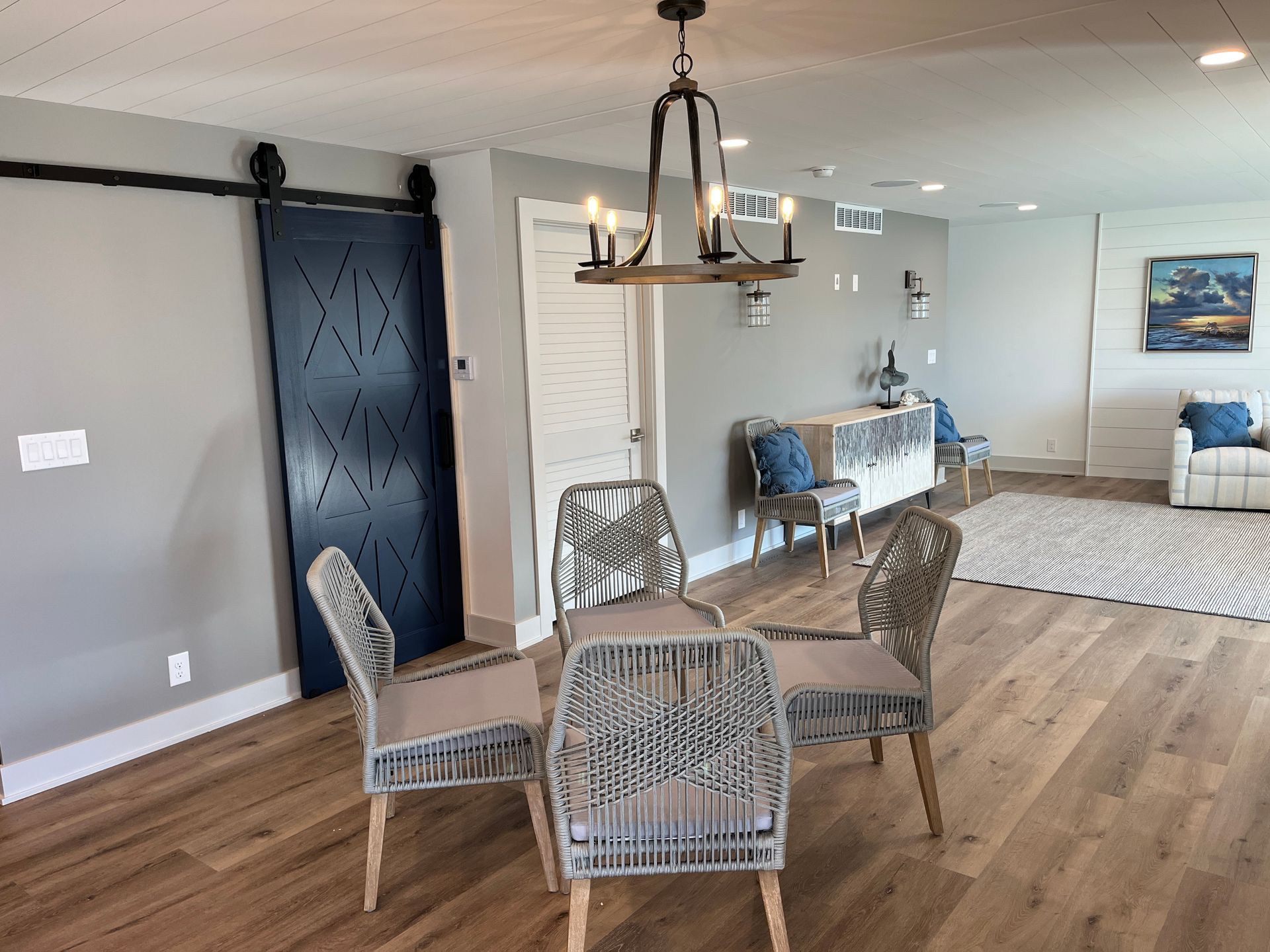 A dining room with a wood floor, a round table with four woven chairs, a blue barn door, and a chandelier.