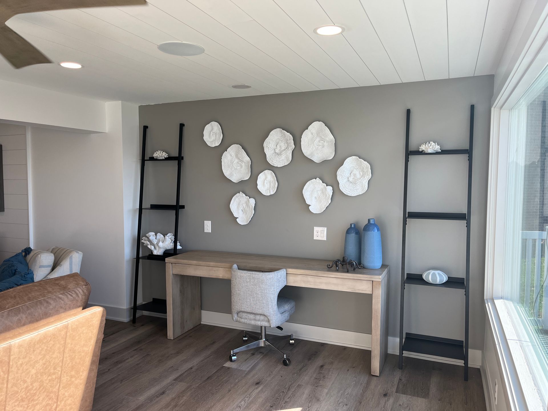 A home office featuring a desk, two black ladder shelves, and white abstract wall art against a gray wall.