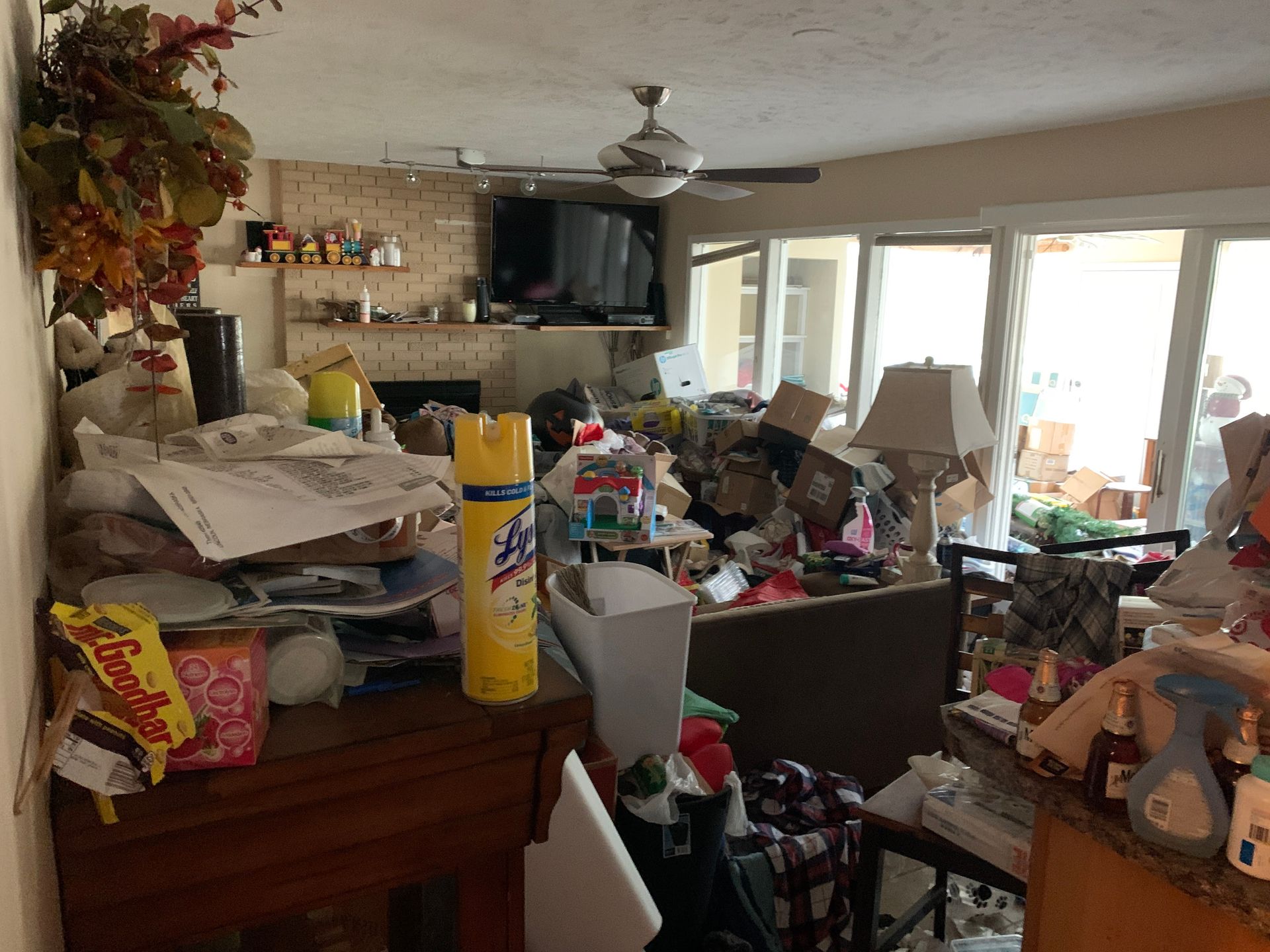 Cluttered living room with piles of items on furniture and surfaces.