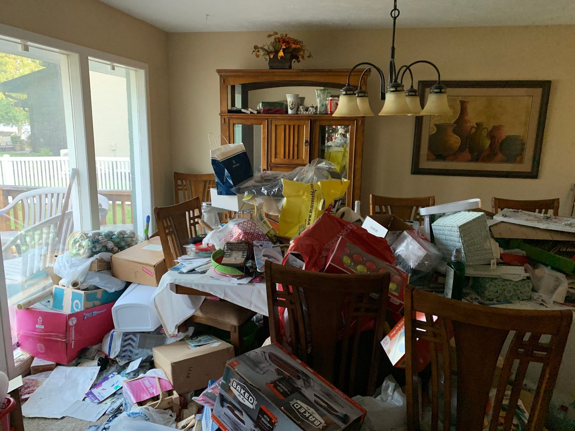 A cluttered dining room table overflowing with boxes and assorted items, with chairs surrounding it.