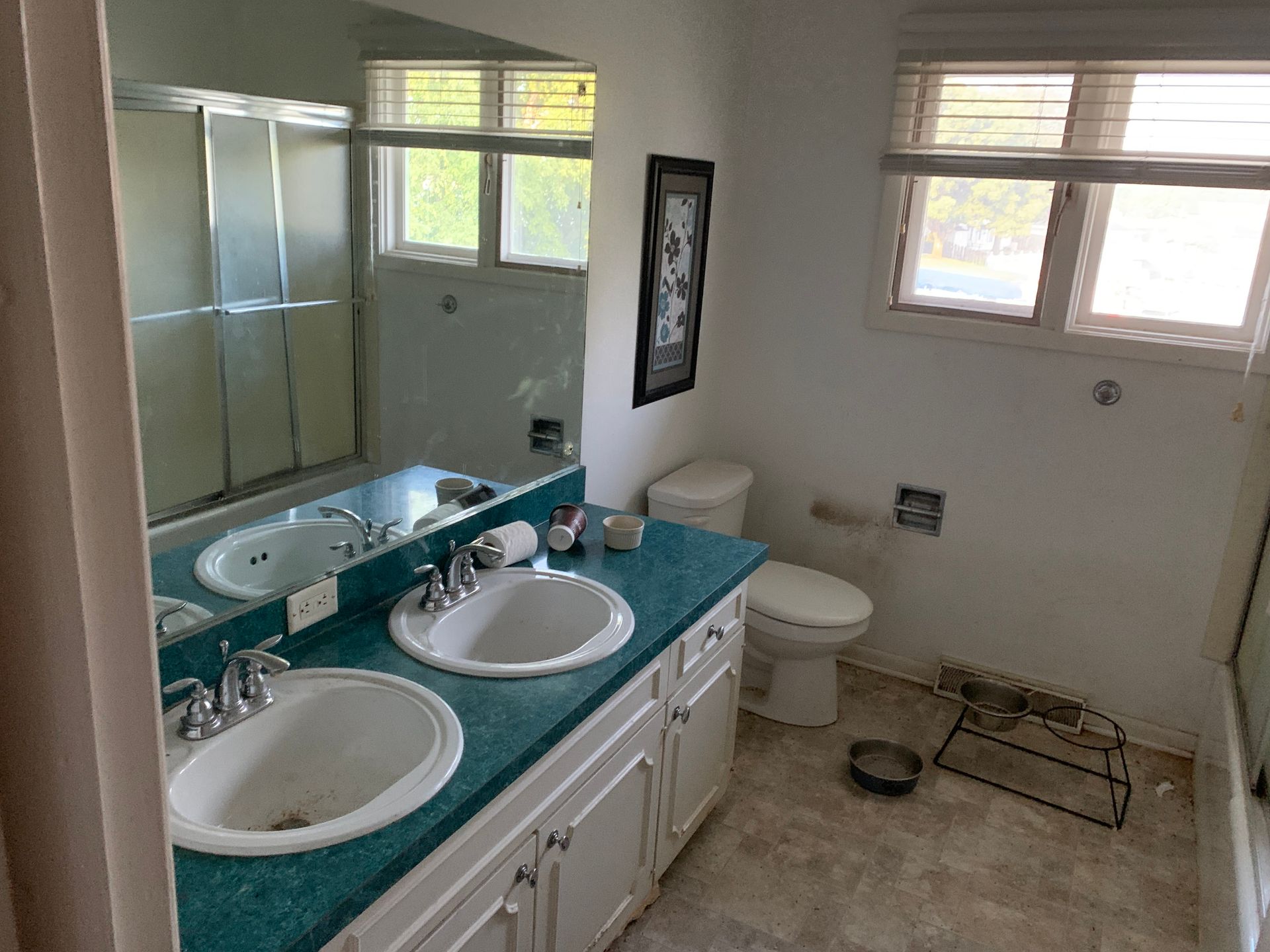 Bathroom with a double sink vanity, a toilet, and a shower/tub combo. White walls, turquoise countertop, and a window.