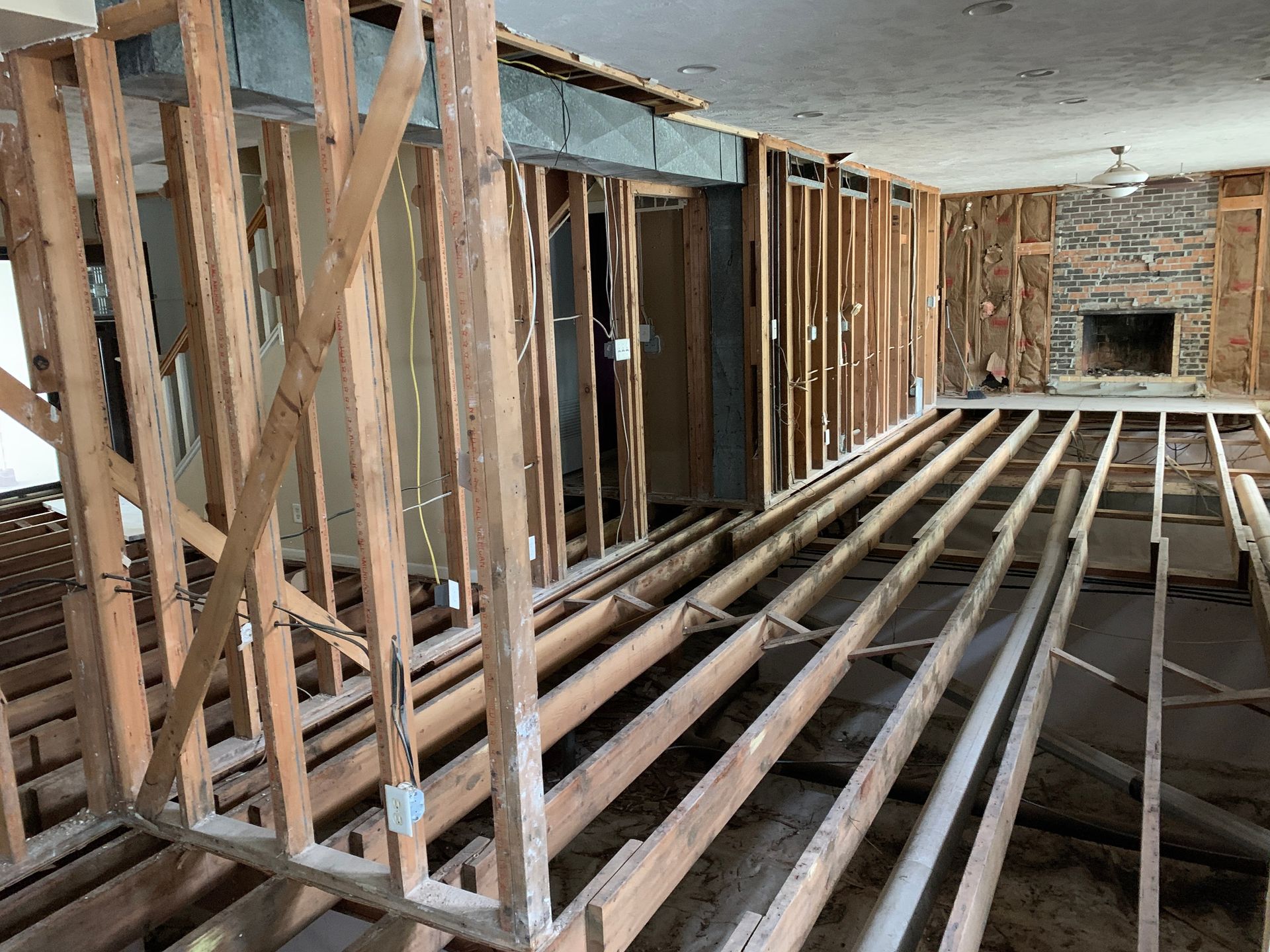 Interior of a home under renovation. Exposed wooden framing of walls and flooring; fireplace in the distance.