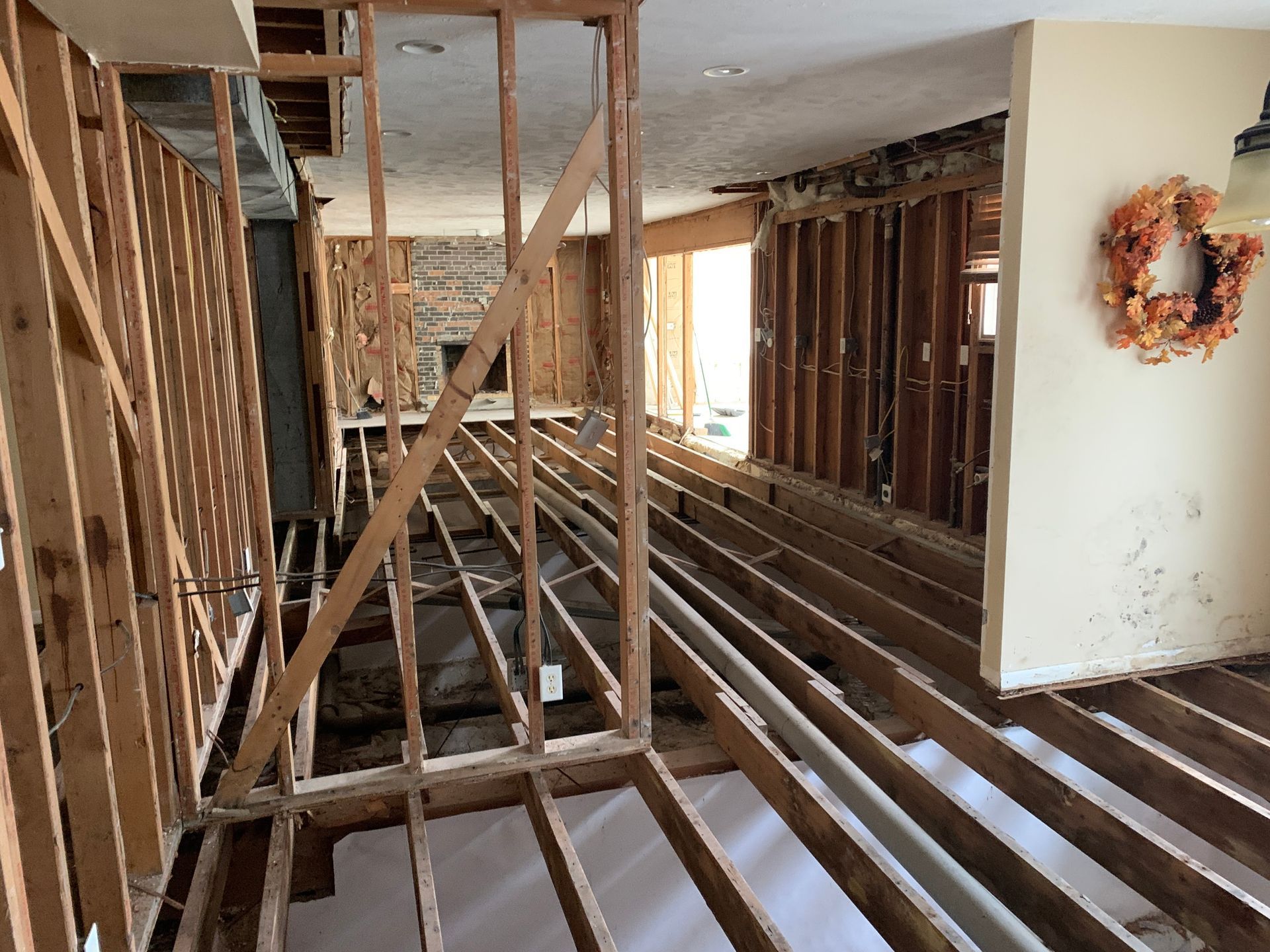 Interior view of a home undergoing renovation. Walls are stripped to the wooden studs, exposing the floor joists and framing.
