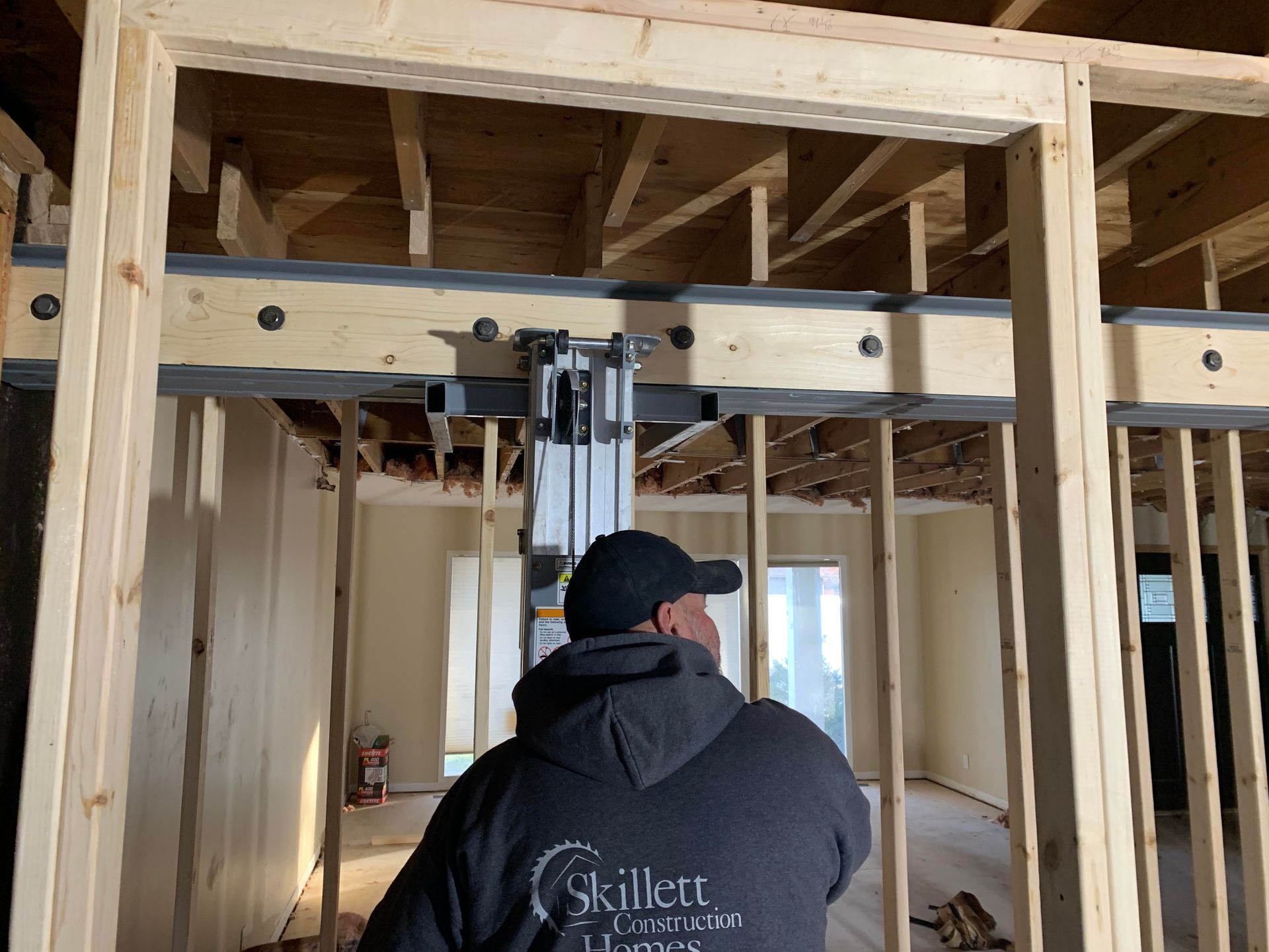 A person wearing a black cap and hoodie looks at a steel beam being installed in a building frame. 