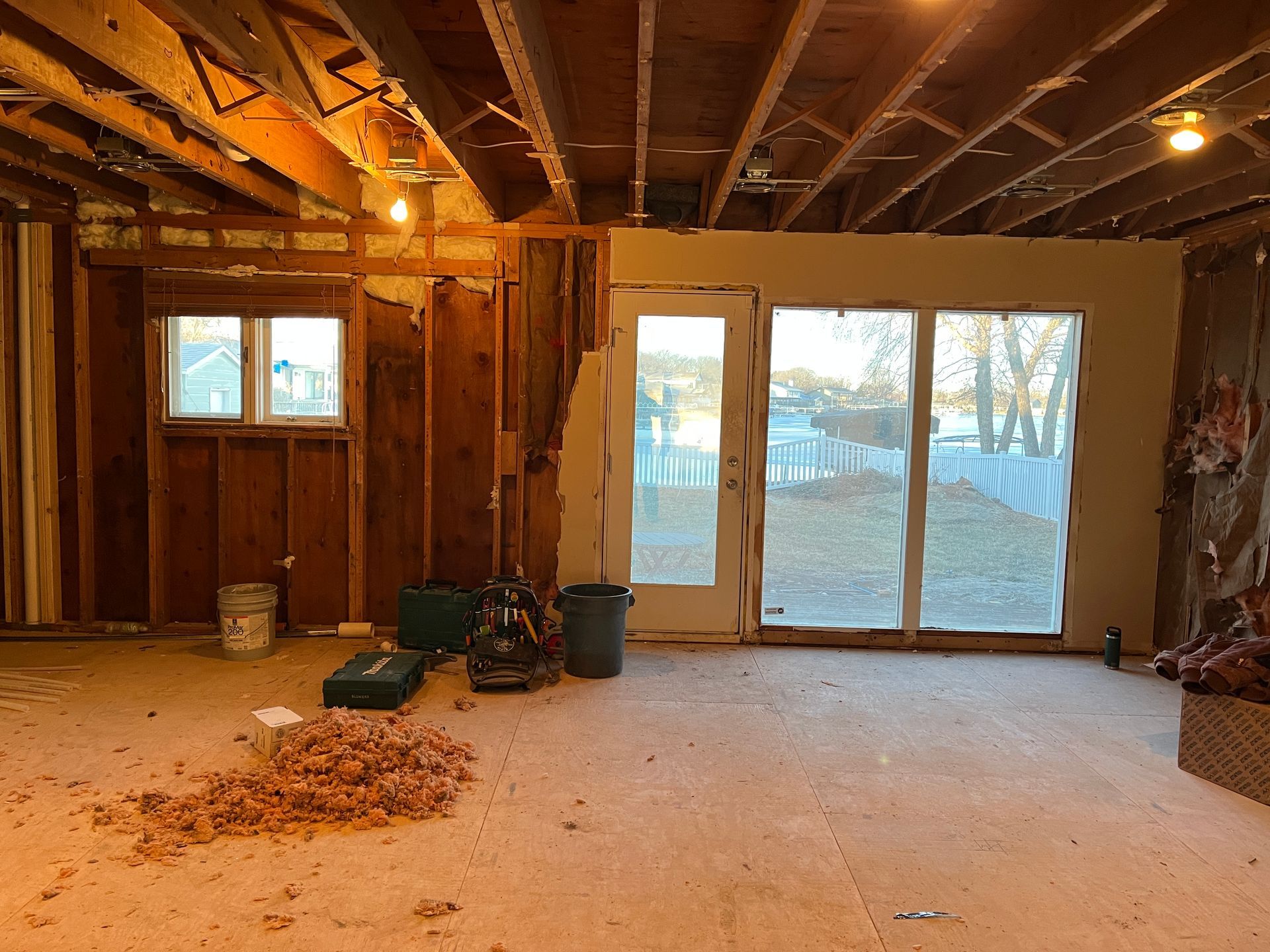 Basement renovation in progress. Exposed framing, and insulation, with a window and sliding glass door leading outside.