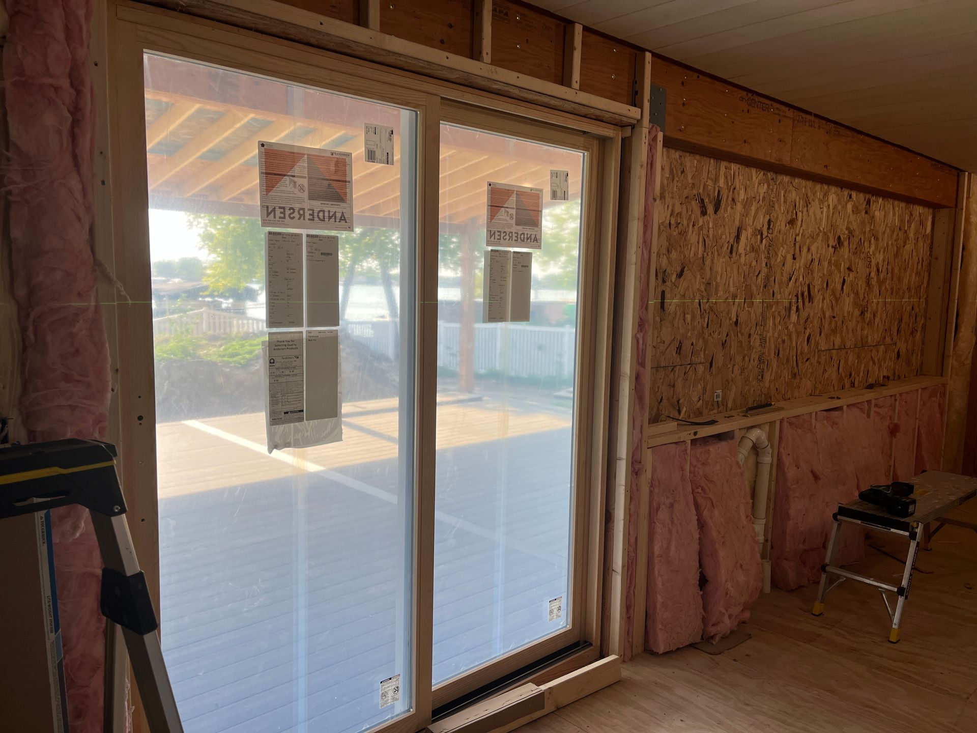 Interior view of a room under construction, showing a large glass door and exposed framing. 