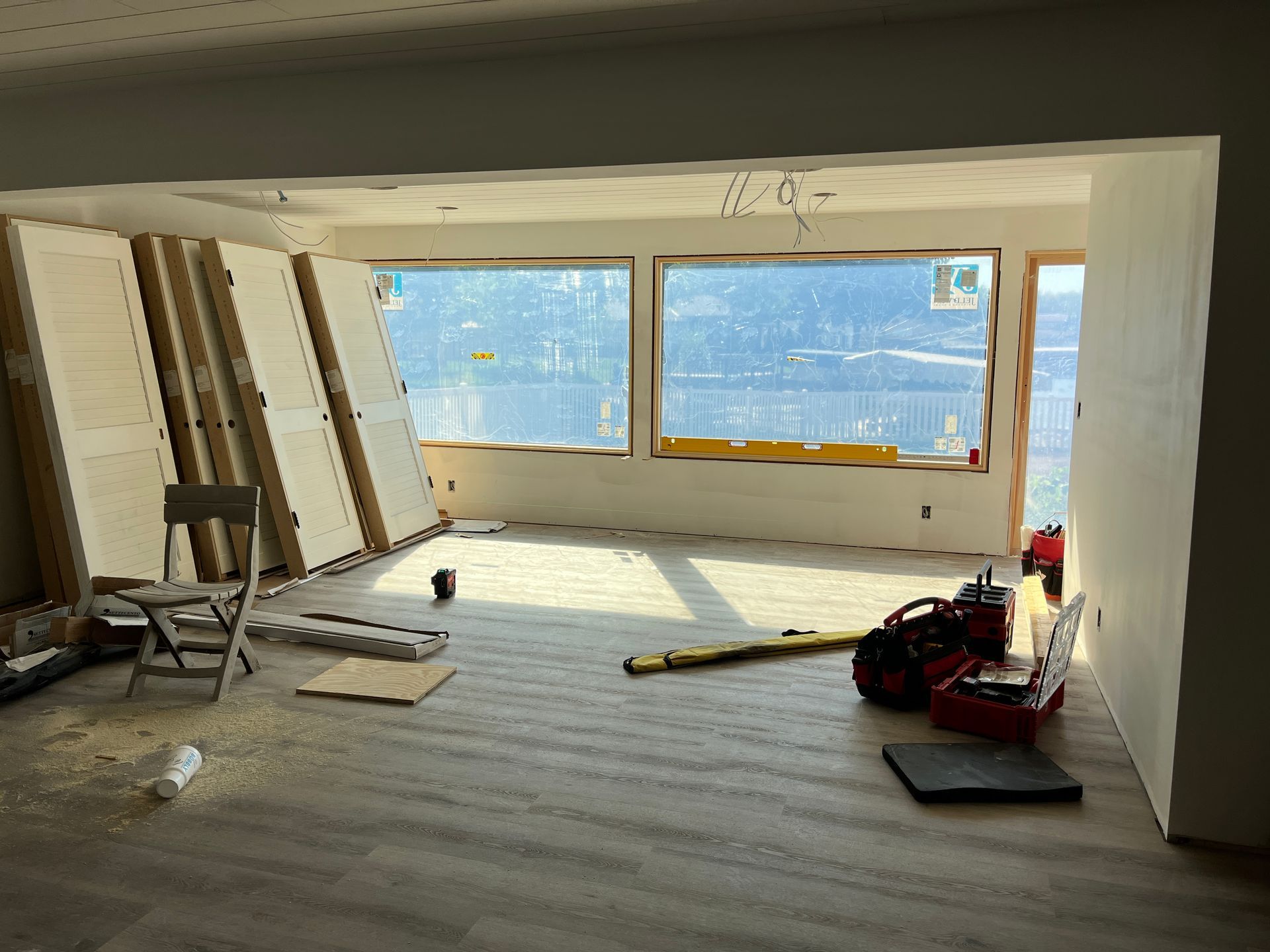 Interior room under construction with large windows; tools and building materials scattered about.
