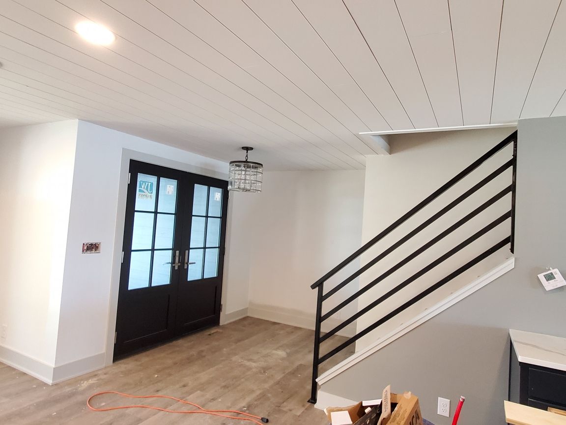 Interior view of a newly renovated space with black French doors, a staircase with black railing, and a wood-plank ceiling.