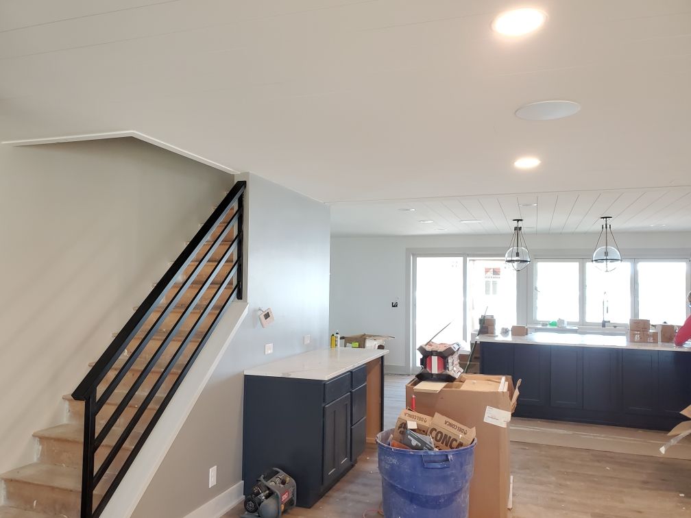 Interior of a home remodel, showcasing a staircase with a black railing, a kitchen with dark cabinets, and unfinished walls.