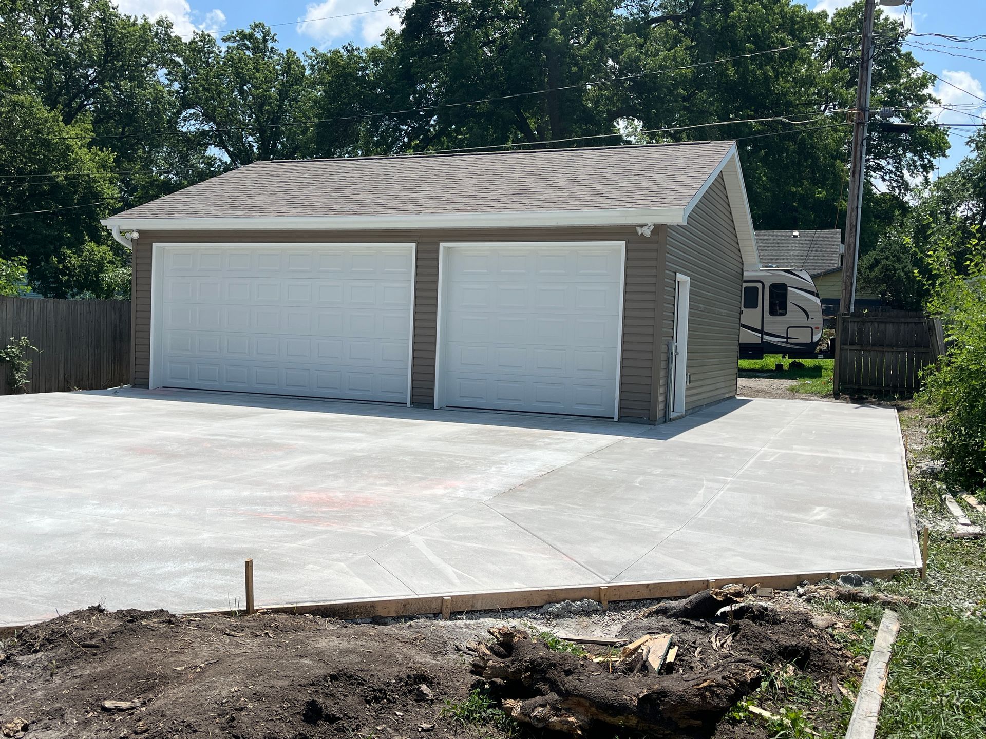 A newly built two-car garage with a concrete driveway. The building has light-colored siding and white garage doors.
