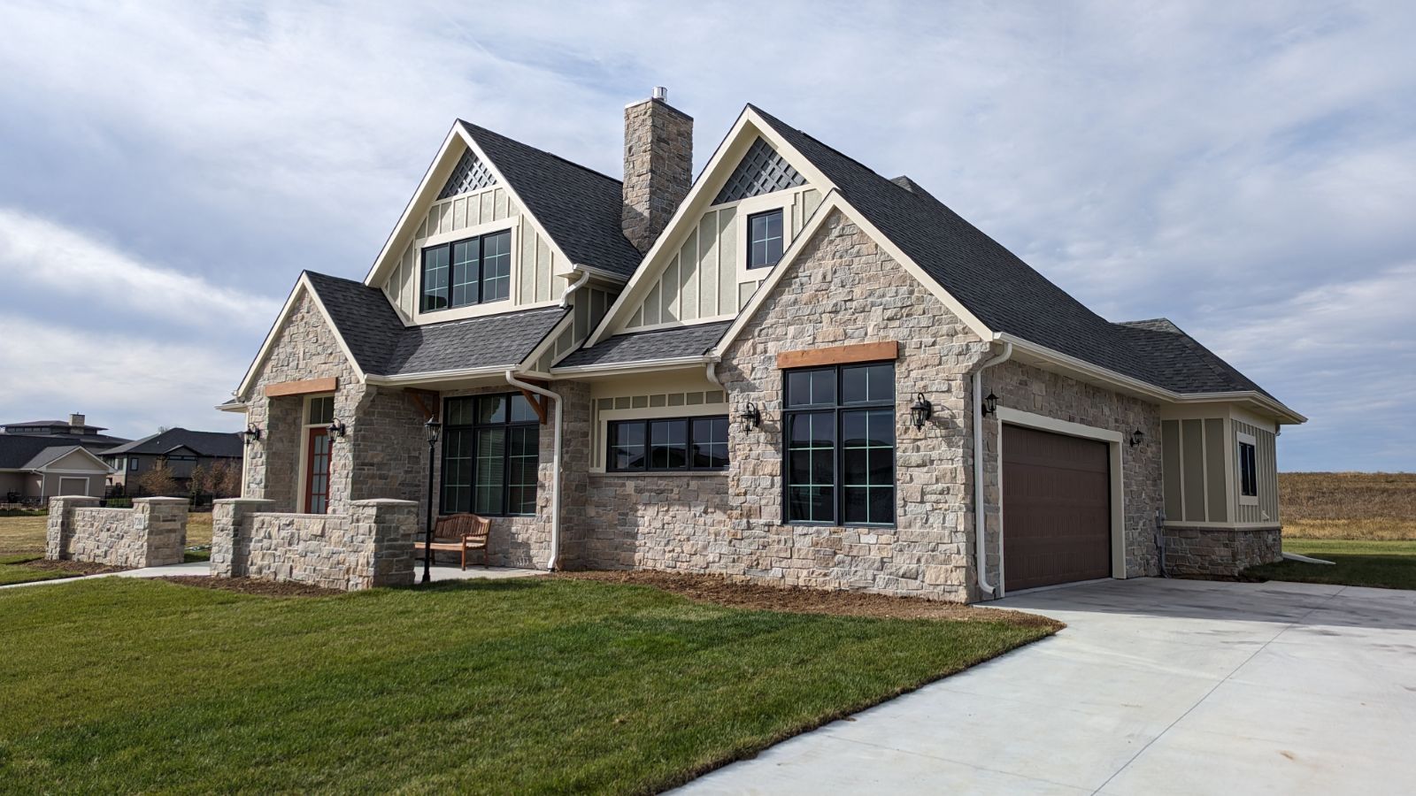 A large stone house with a gray roof and a brown garage door.
