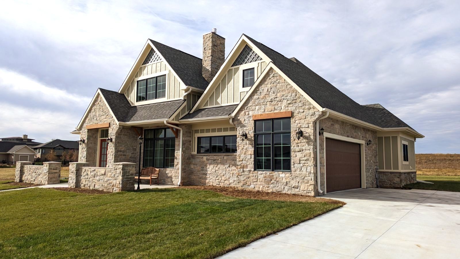 A large house with a garage and a lot of windows is sitting on top of a lush green field.
