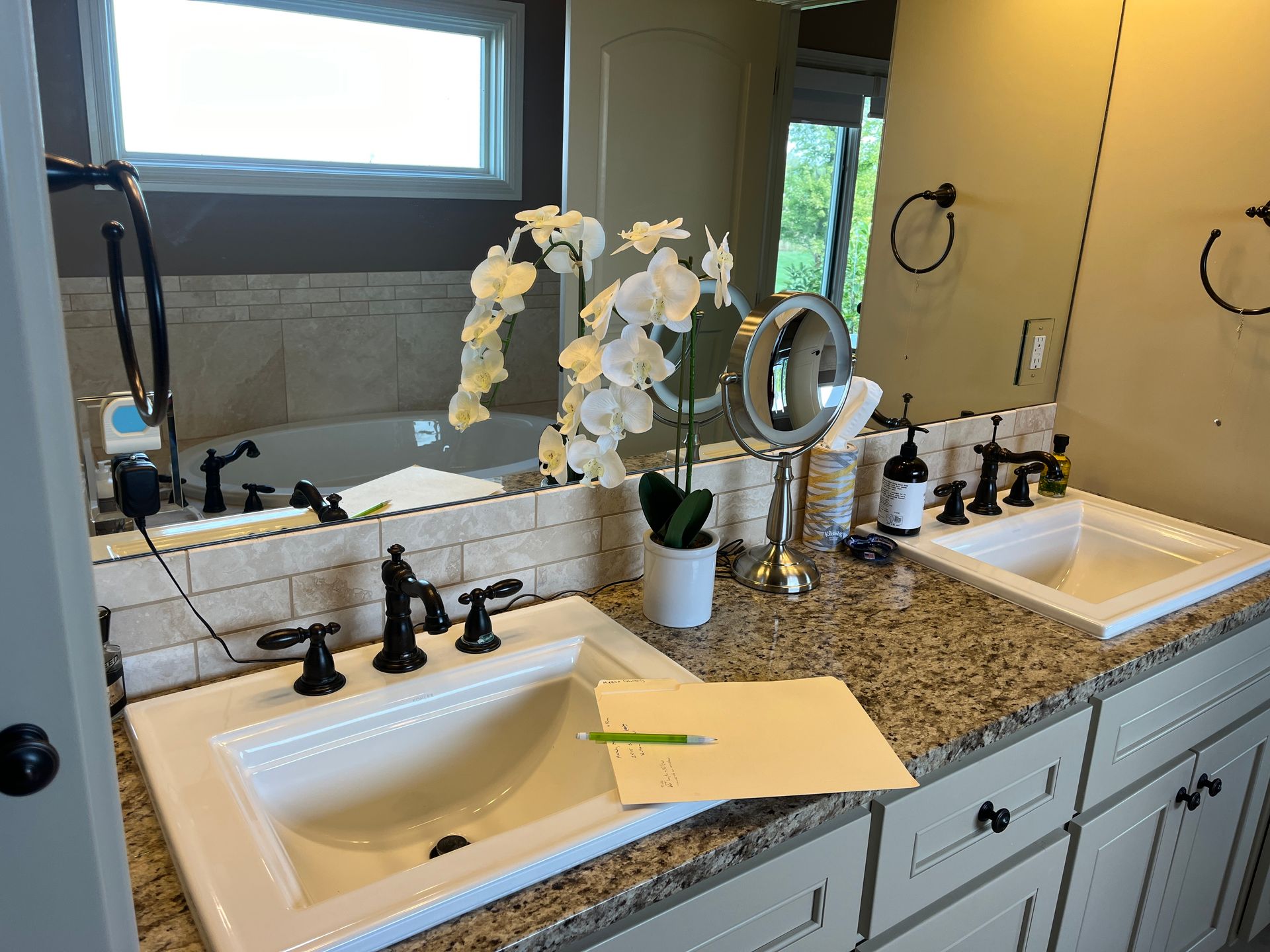Bathroom with dual sinks, granite countertop, large mirror, and decorative orchids.