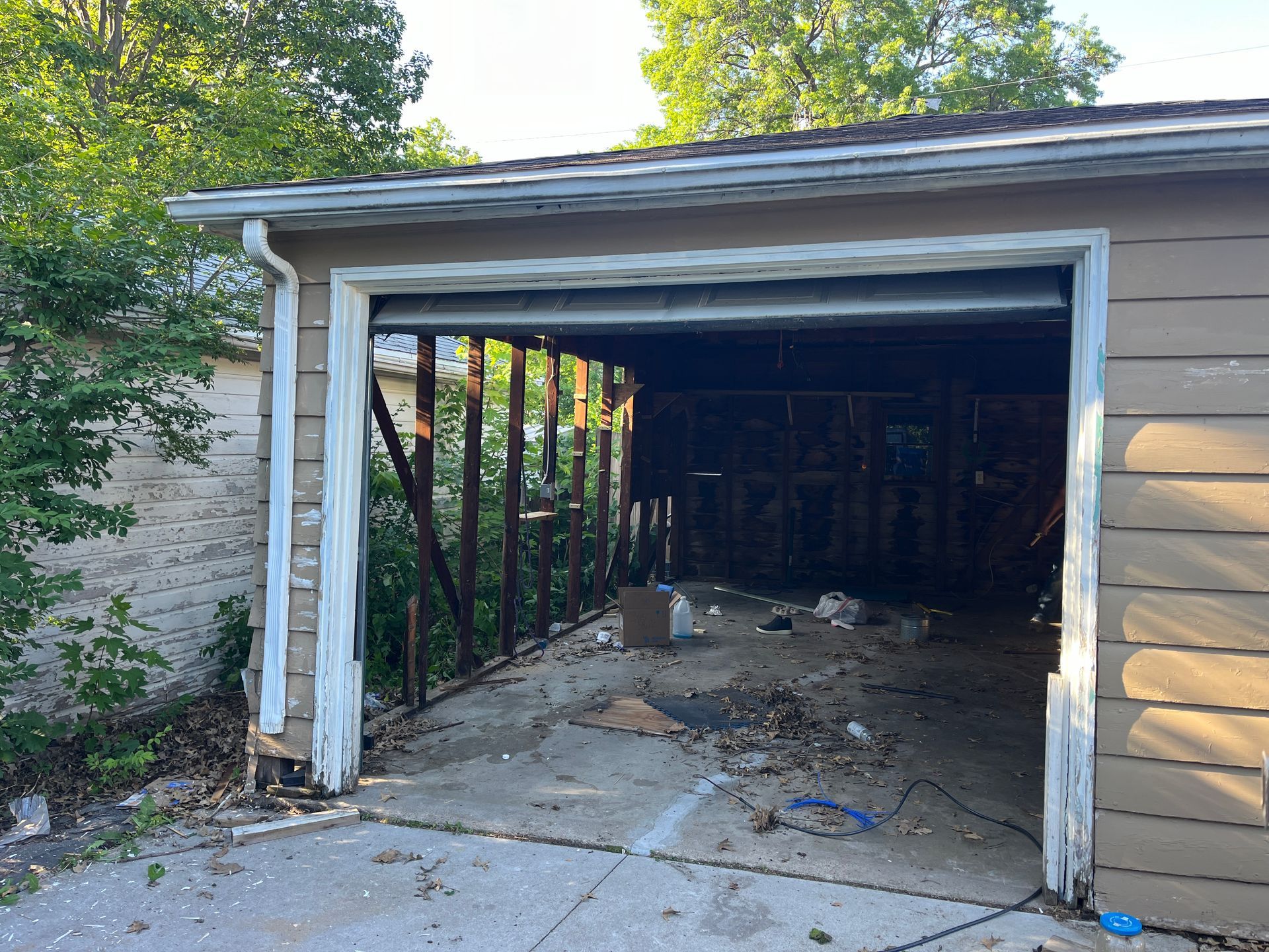 Exterior view of a damaged garage with an open doorway, revealing exposed wooden beams and debris.