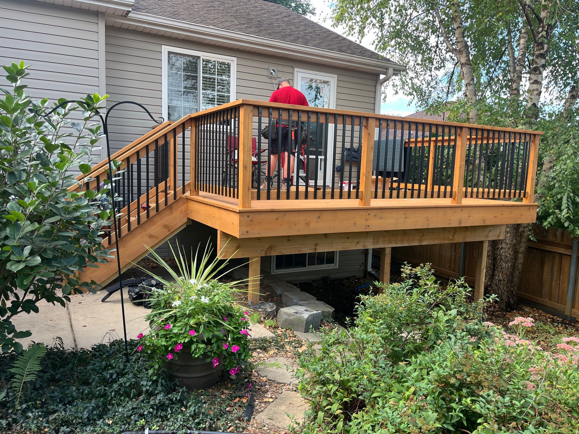 A man is standing on a wooden deck in front of a house.