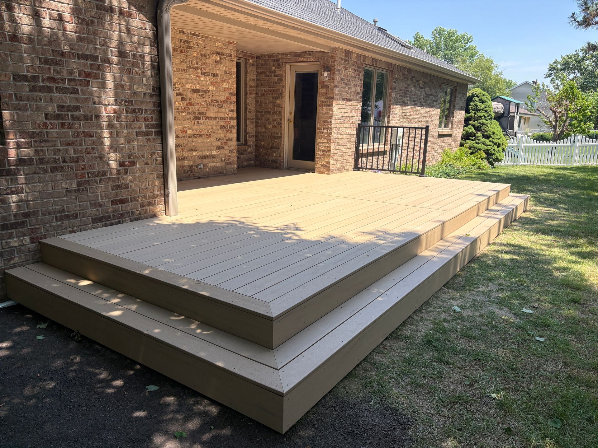 Wooden deck with steps in front of a brick house, on a sunny day.