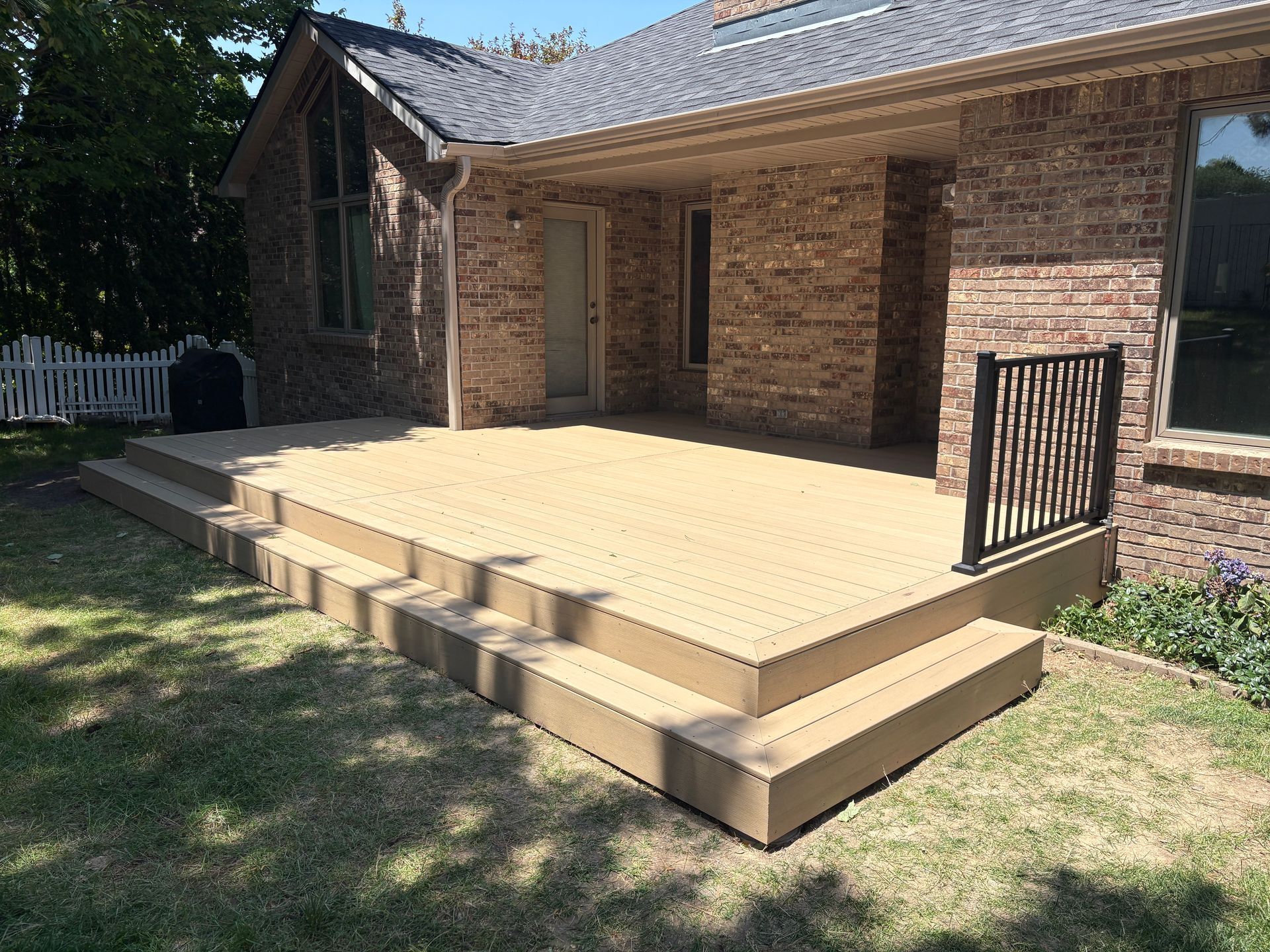 A brick house with a composite deck and steps, brown railings, and green grass.