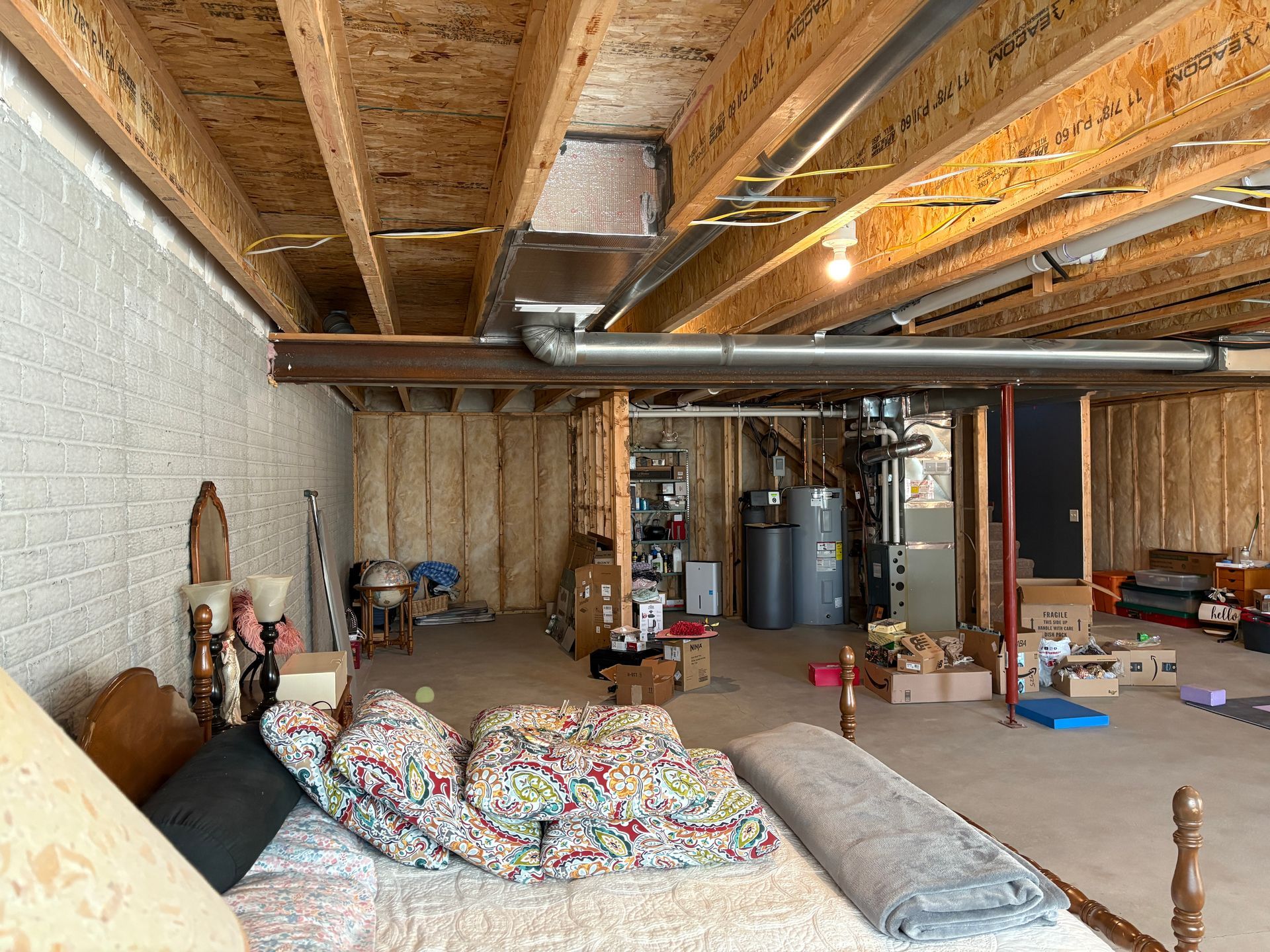 Unfinished basement with exposed beams, insulation, and various stored items.