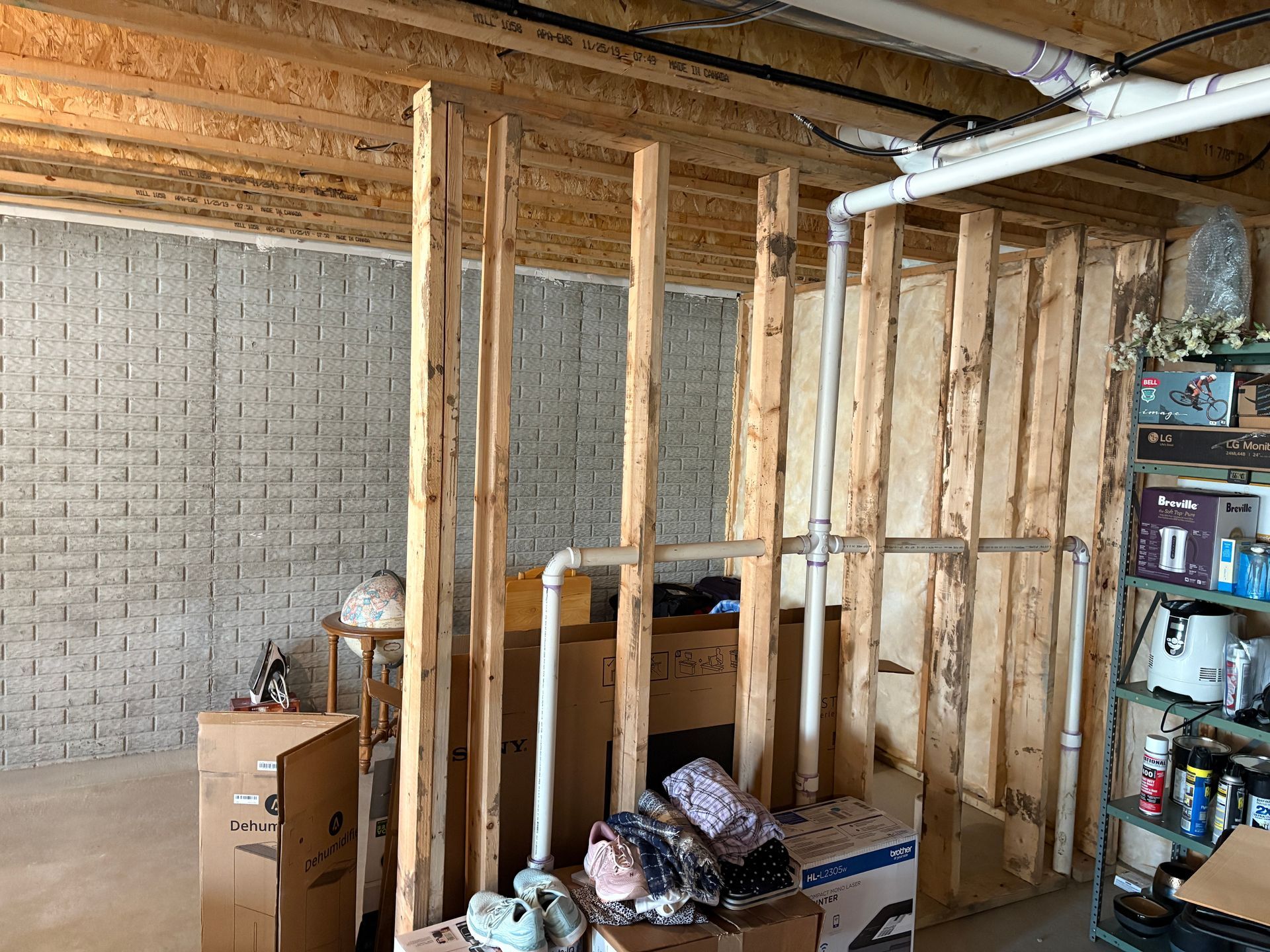 Basement framing with exposed insulation and brick wall. Pipes, boxes, and miscellaneous items are present.