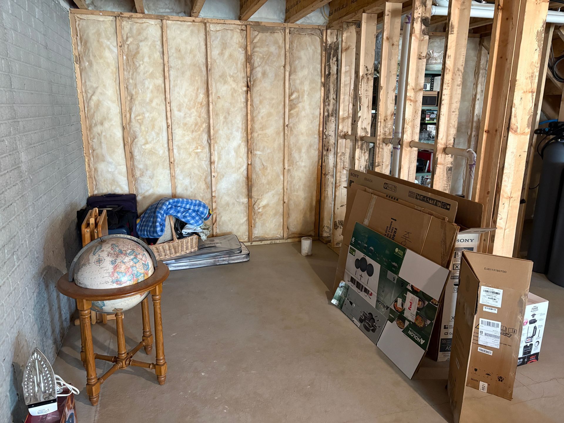 Basement interior with exposed wooden framing, insulation, a globe, boxes, and various items.