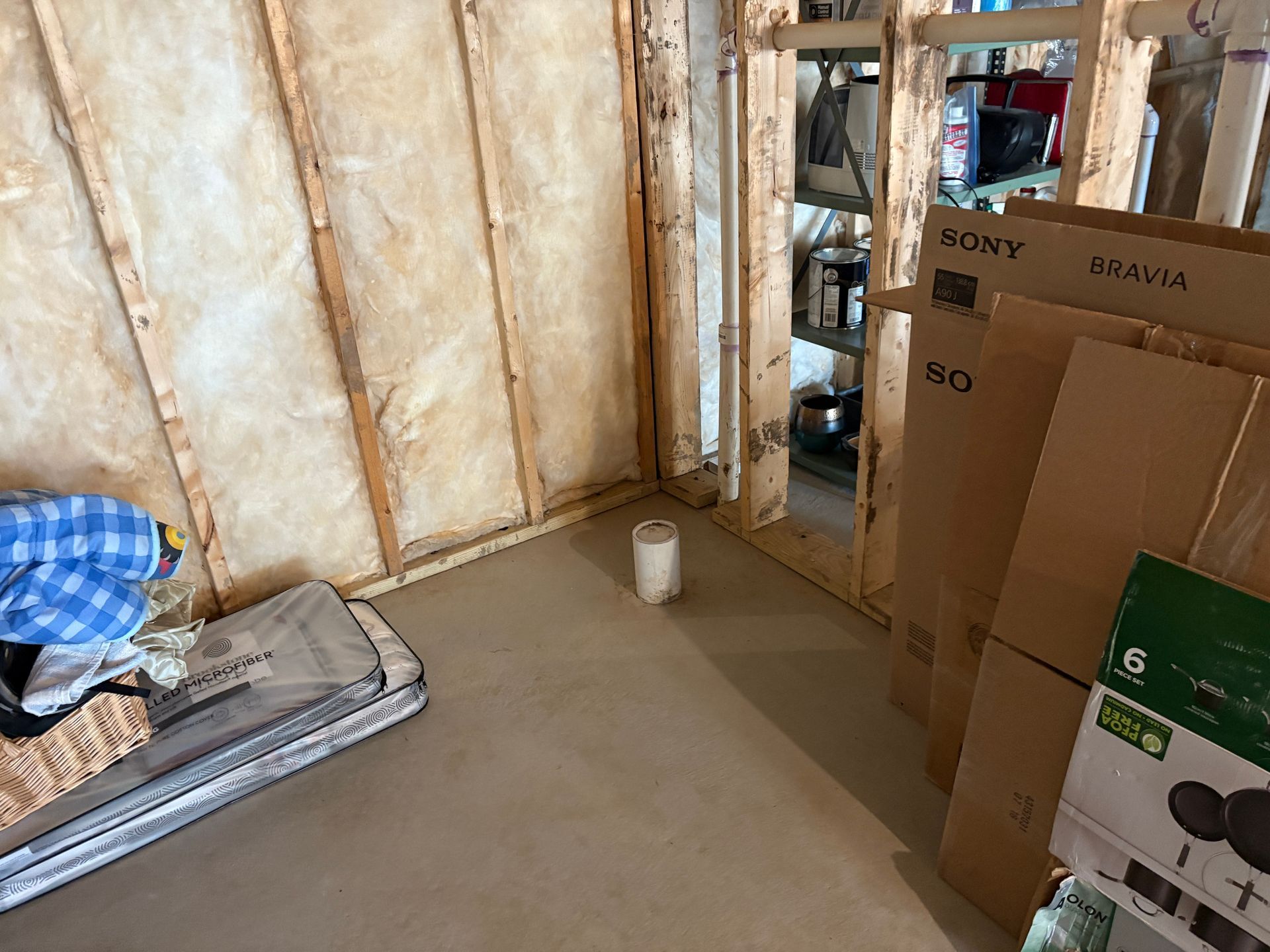 Unfinished basement with exposed studs, insulation, and cardboard boxes. Floor is concrete.