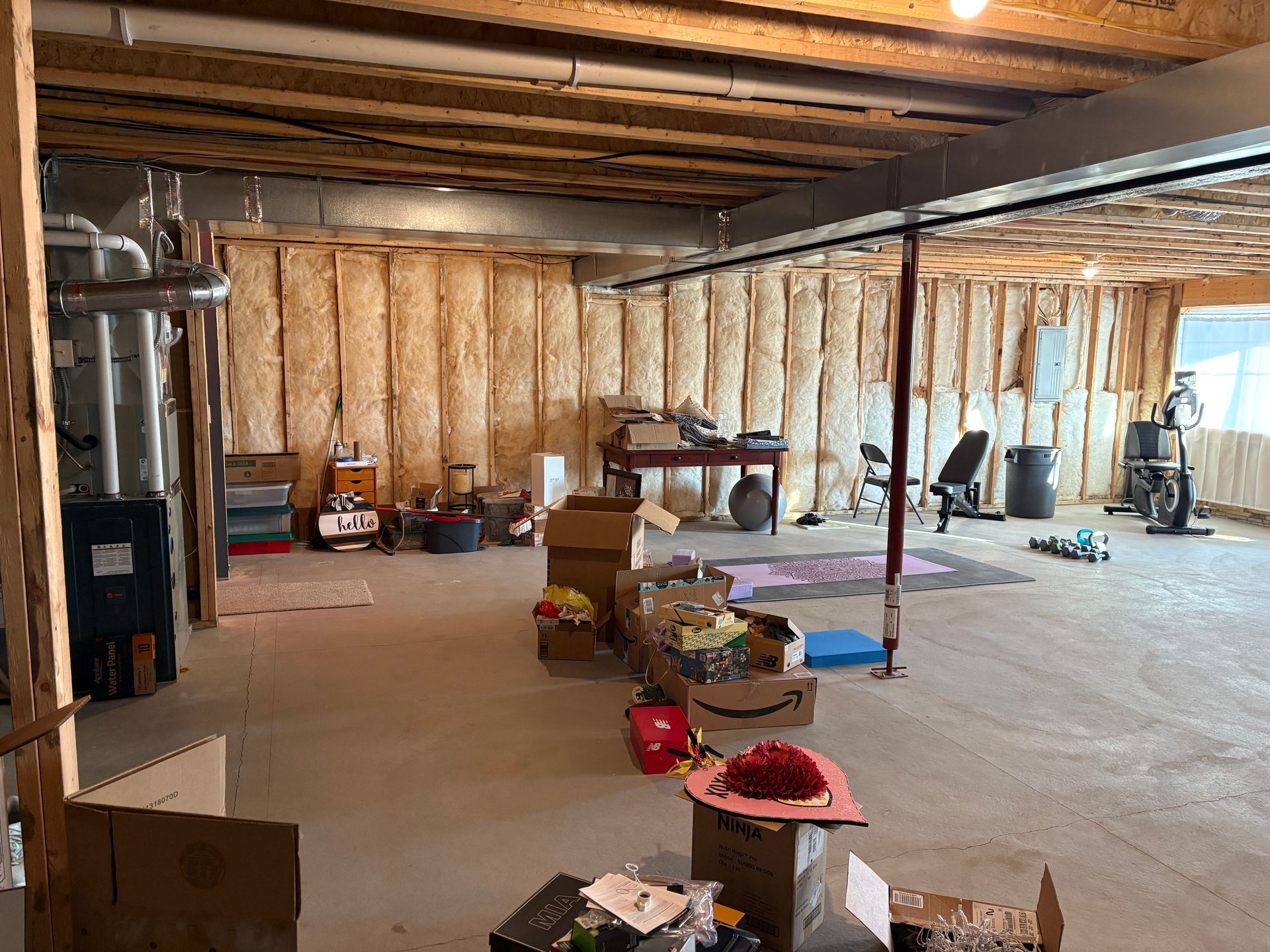 Unfinished basement with exposed insulation, boxes, and exercise equipment.