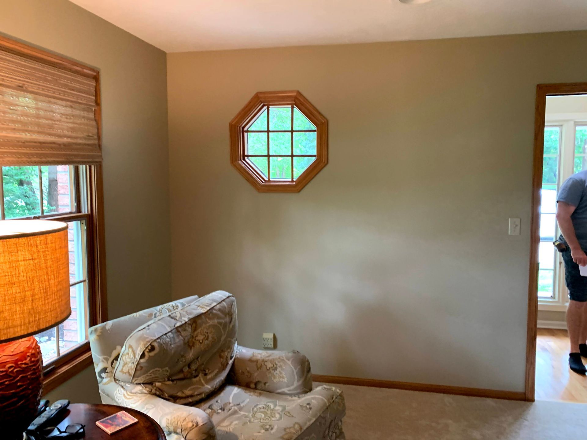 Interior view of a room with an octagonal window, chair, and doorway. Earth-toned walls and window trim.