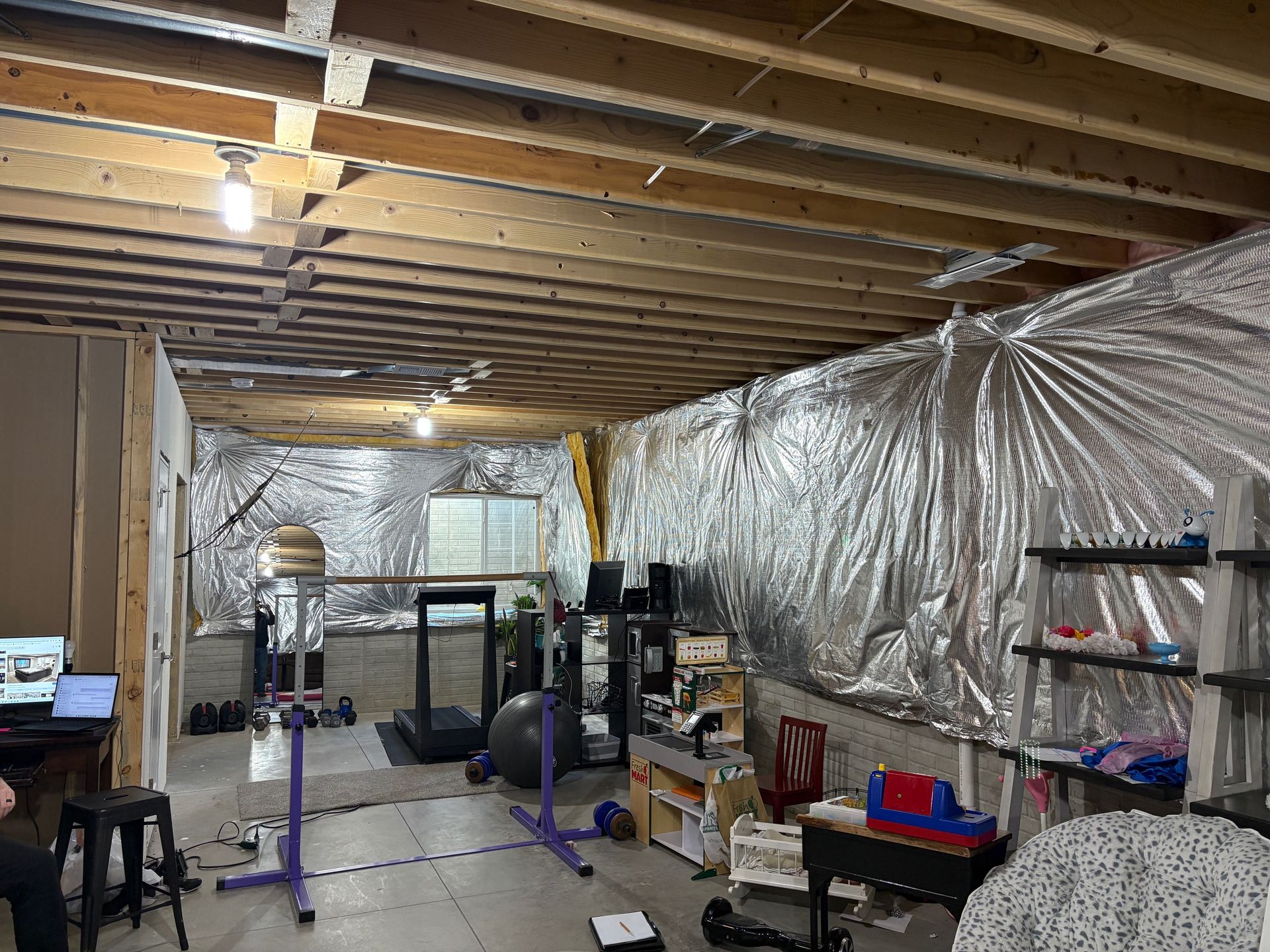 Basement gym with exercise equipment, computers, and reflective insulation on walls.