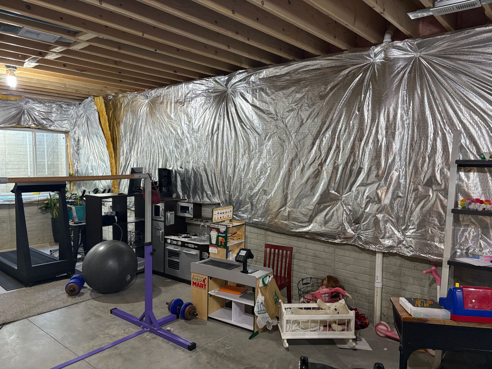 Basement with silver insulation on the wall, exercise equipment, and storage.