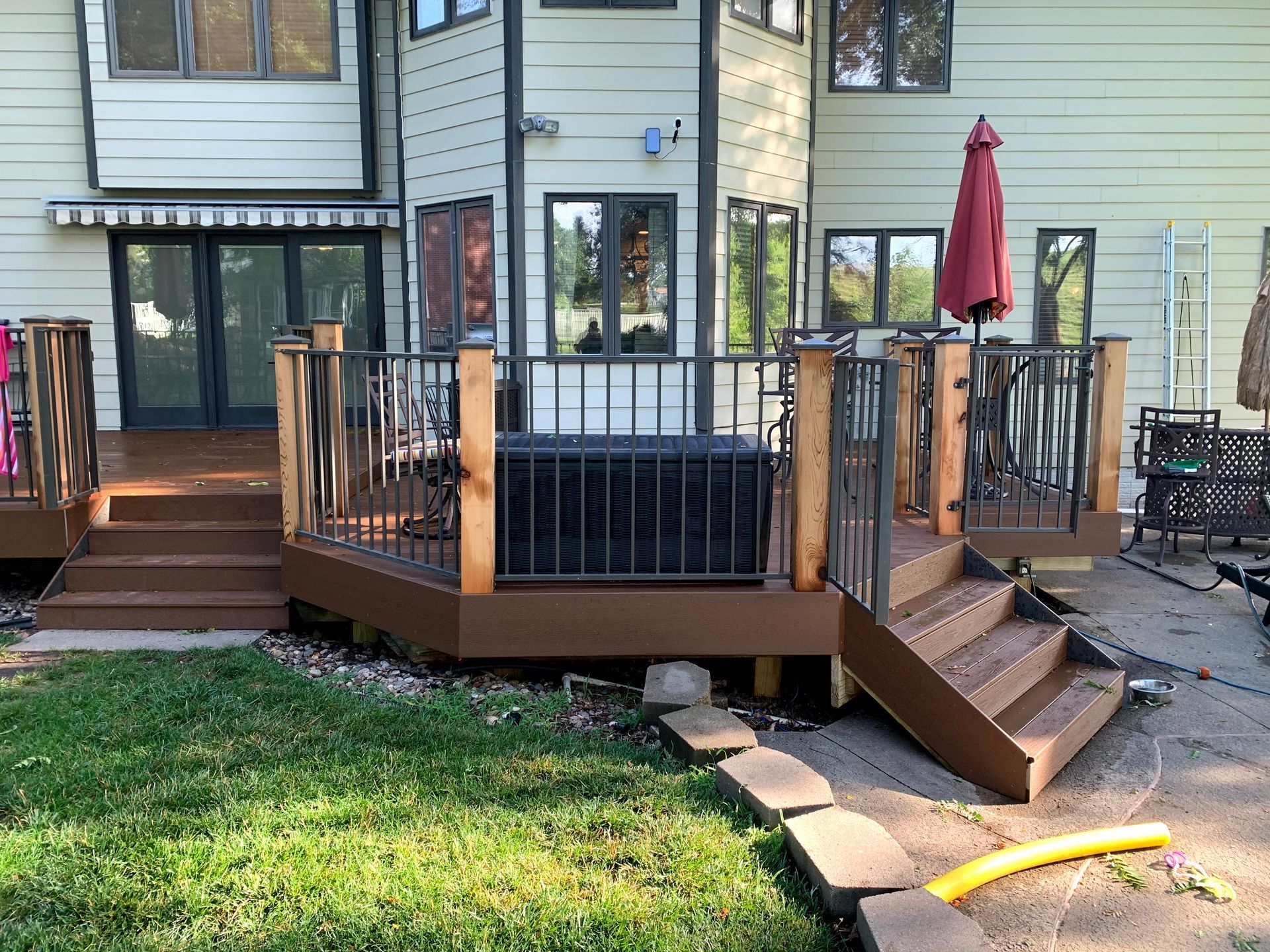 A wooden deck with stairs and a red umbrella in front of a house.