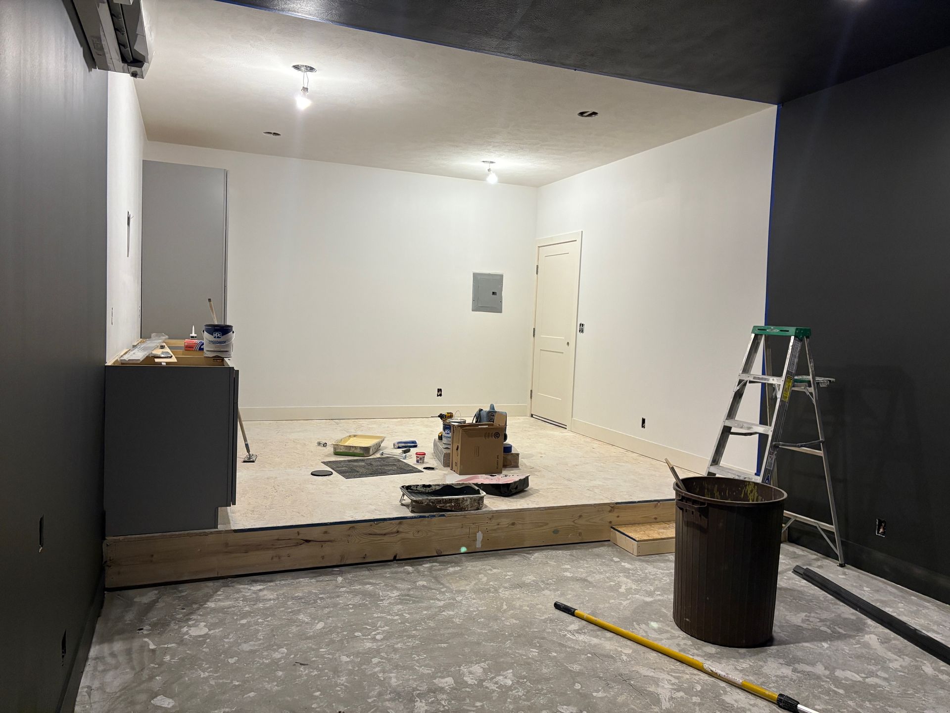 A room that is being remodeled with a ladder and a trash can on the floor.