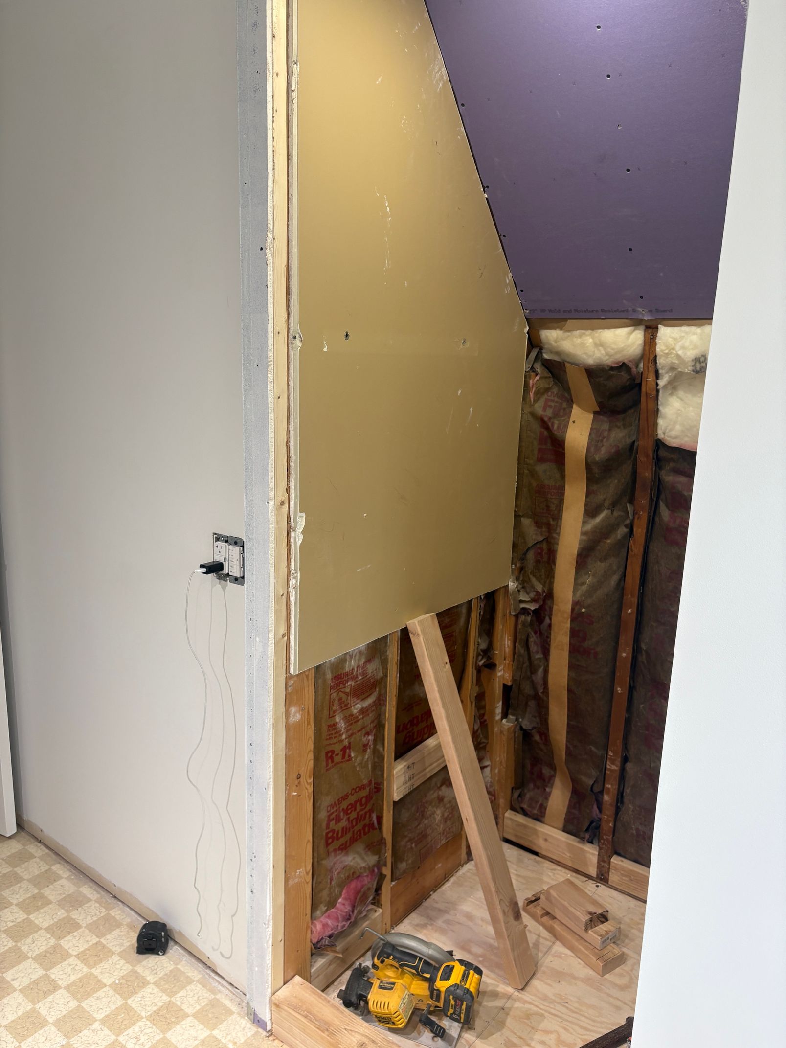 Construction of a doorway. Yellow drywall and exposed framing with insulation visible. A power tool sits on the floor.