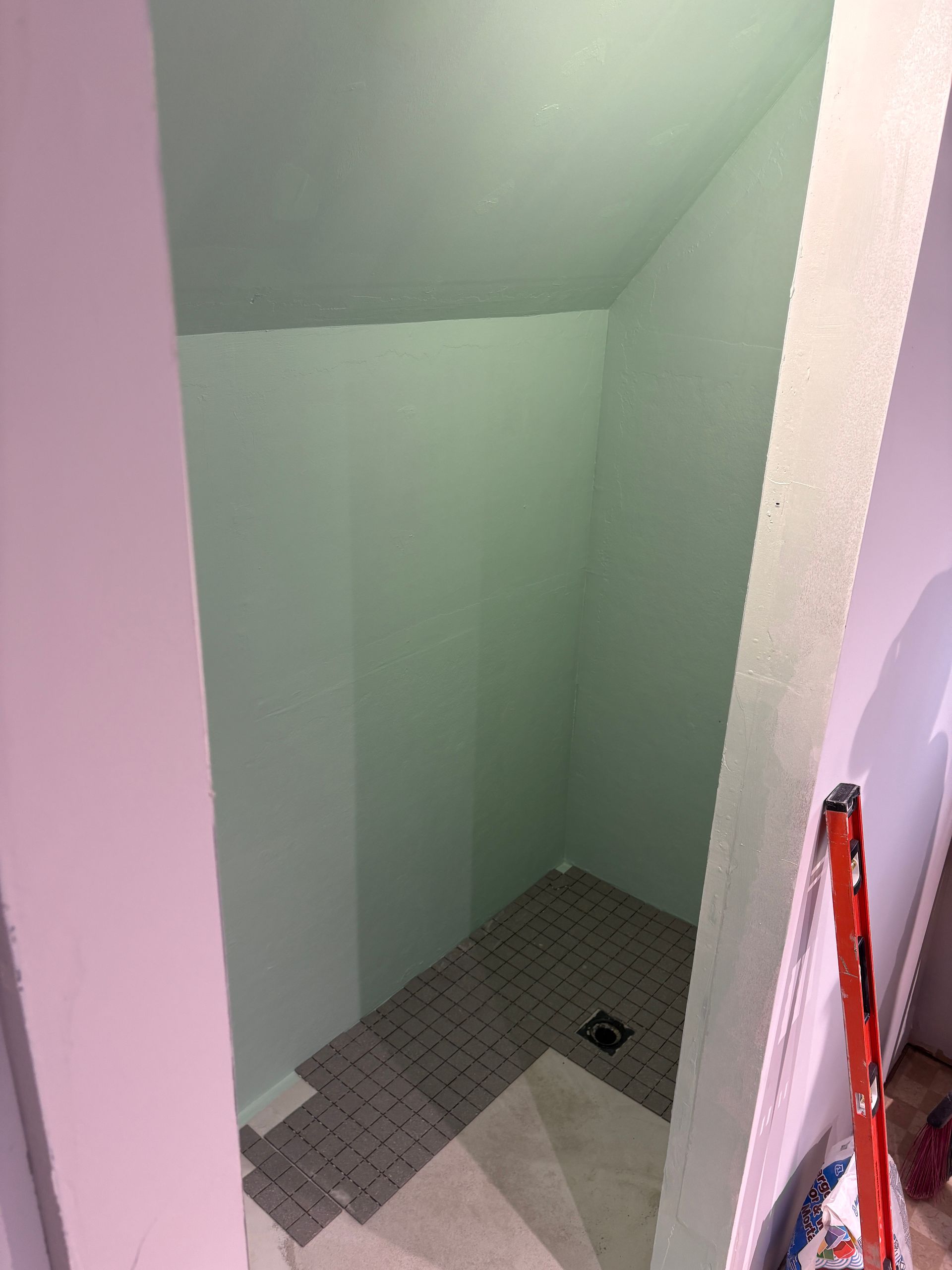Small, narrow, unfinished bathroom, light green walls, grey tiled floor, white trim, pink doorway.