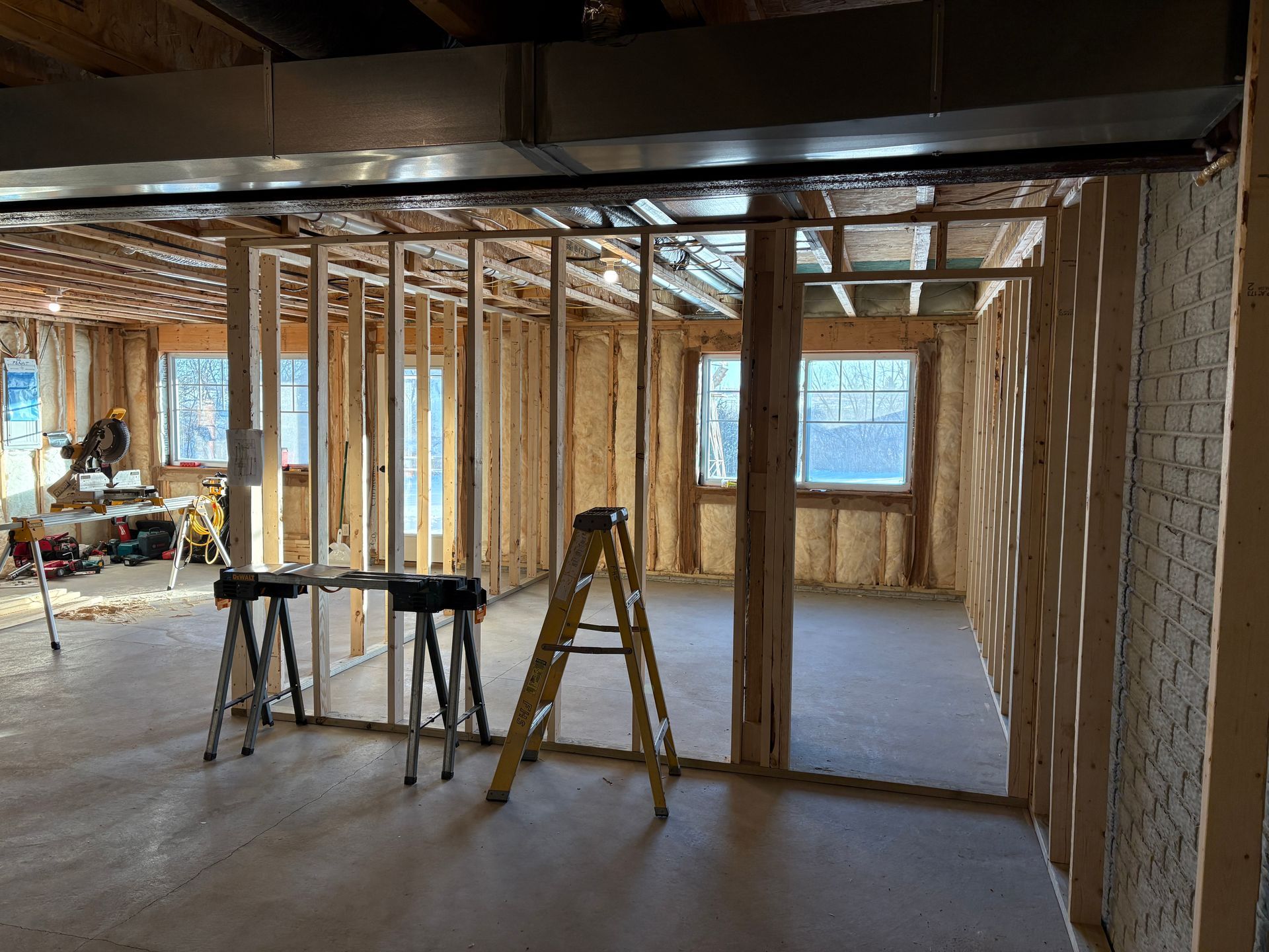 Interior view of a basement under construction with wooden studs, windows, and tools.